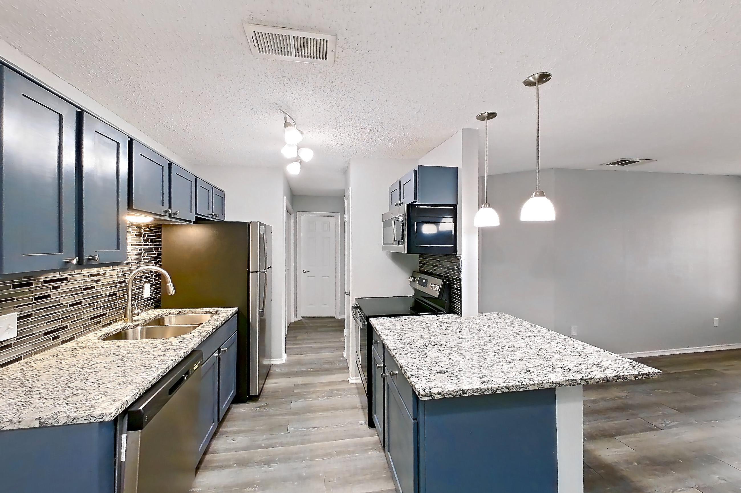 Dining room with dark wood-finish flooring, dishwasher, electric range, fireplace, light countertops, light stone countertops, light wood-finish flooring, oven/range, refrigerator, and stainless steel appliances, Apartment 2302 at Quail Ridge Apartments