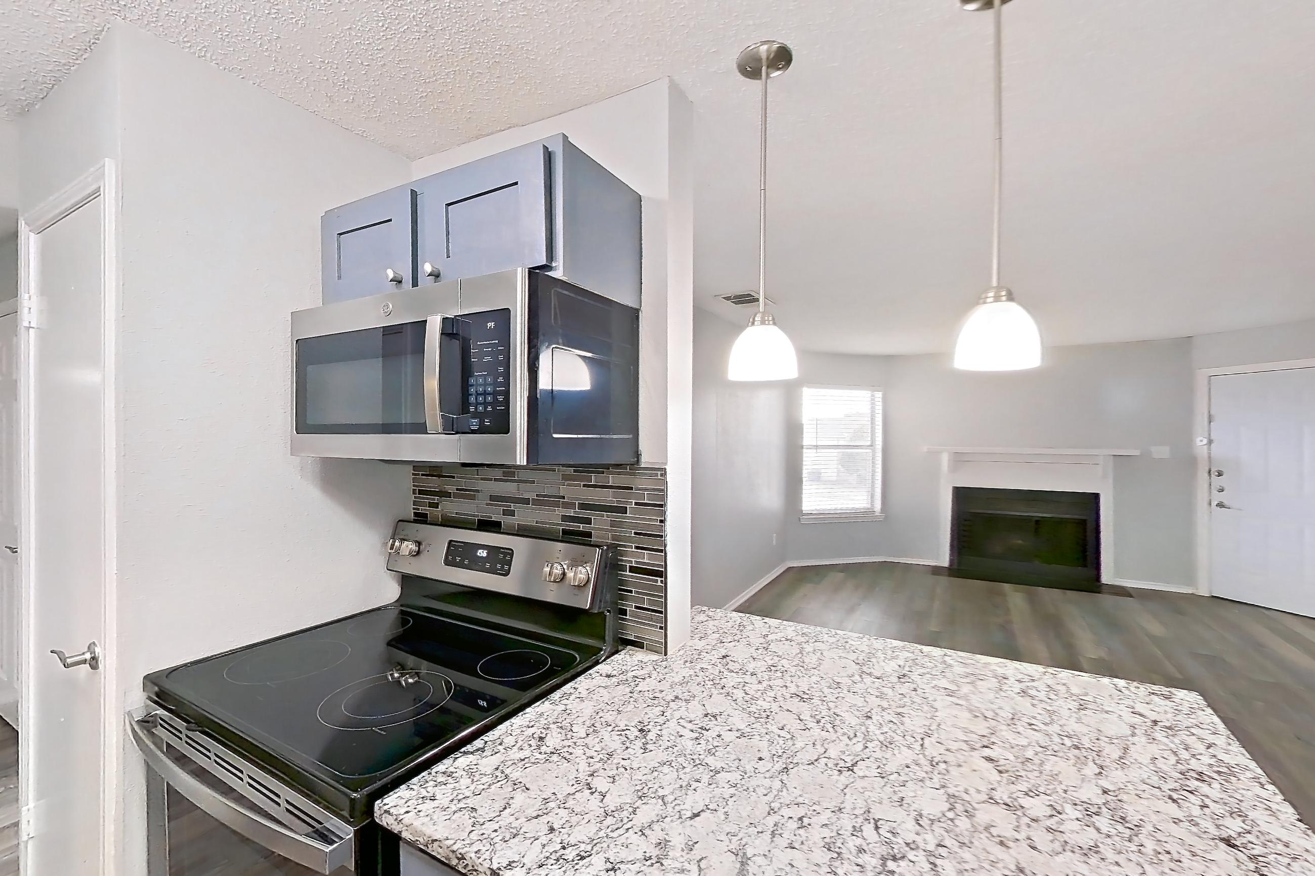 Kitchen with dishwasher, electric range, fireplace, light countertops, light stone countertops, light wood-finish flooring, oven/range, refrigerator, and stainless steel appliances, Apartment 2302 at Quail Ridge Apartments