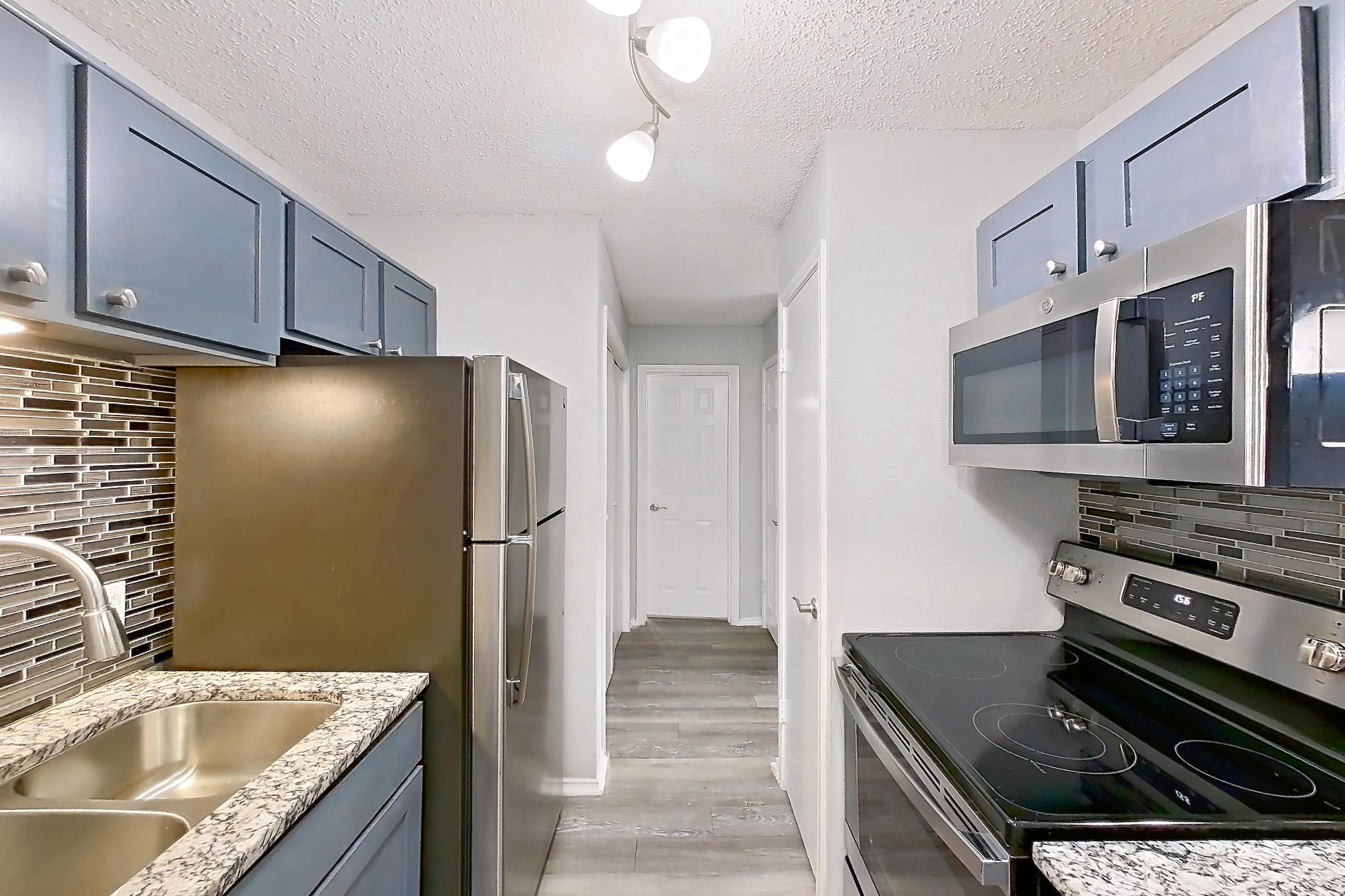 Kitchen with dishwasher, electric range, fireplace, light countertops, light stone countertops, light wood-finish flooring, oven/range, refrigerator, and stainless steel appliances, Apartment 2302 at Quail Ridge Apartments