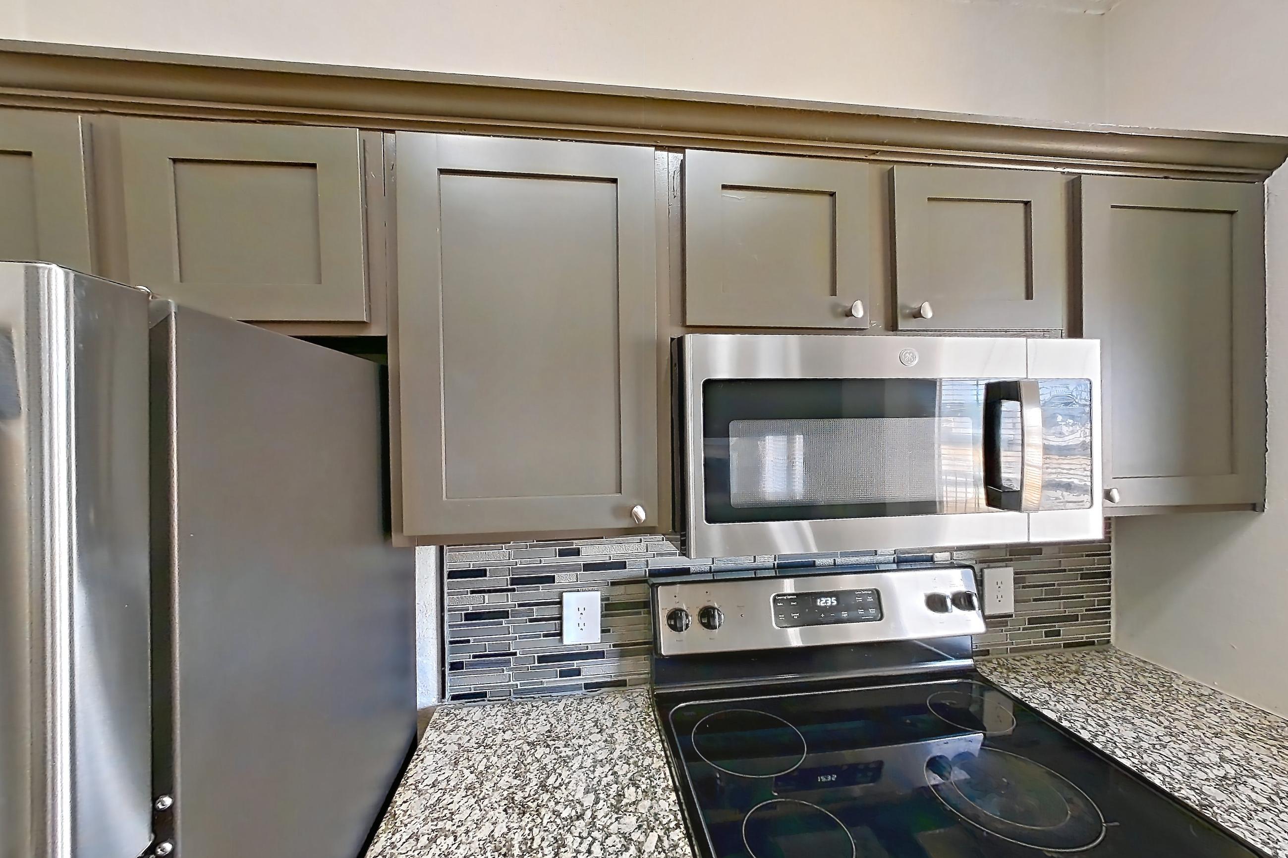 Kitchen with dishwasher, light countertops, light stone countertops, light wood-finish flooring, refrigerator, and stainless steel appliances, Apartment 1522 at Waterford on the Meadow