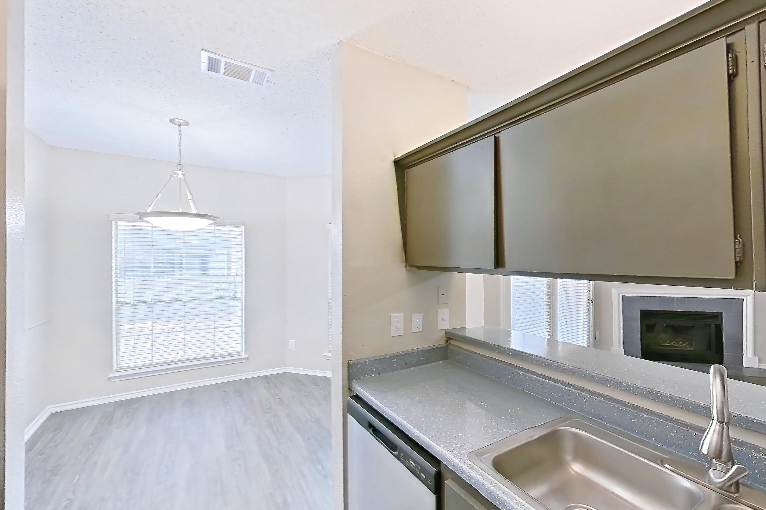 Kitchen with dark countertops, dishwasher, electric range, fireplace, light wood-finish flooring, oven/range, refrigerator, stainless steel appliances, and tile fireplace, Apartment 3013 at Waterford on the Meadow