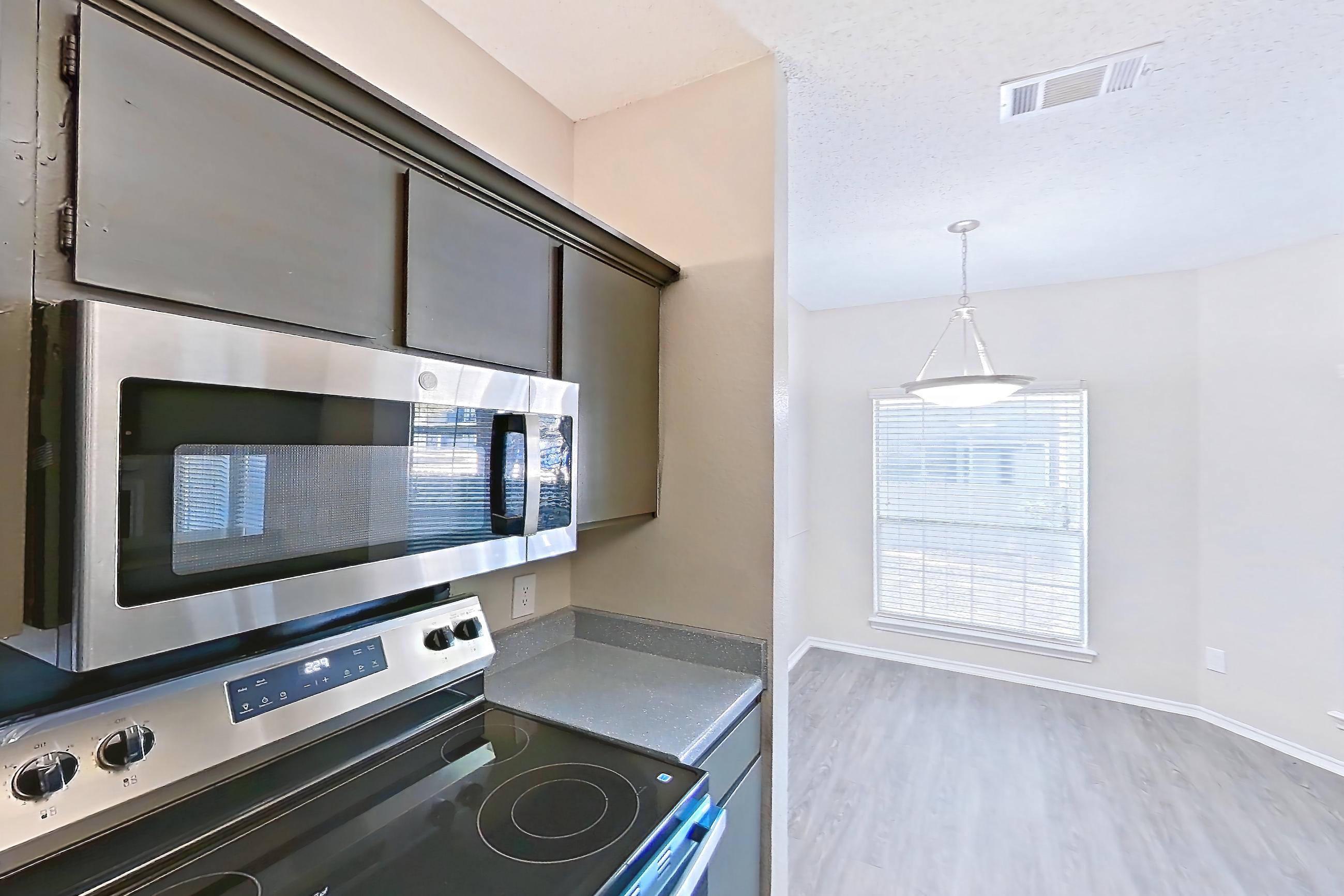 Kitchen with dark countertops, dishwasher, electric range, fireplace, light wood-finish flooring, oven/range, refrigerator, stainless steel appliances, and tile fireplace, Apartment 3013 at Waterford on the Meadow