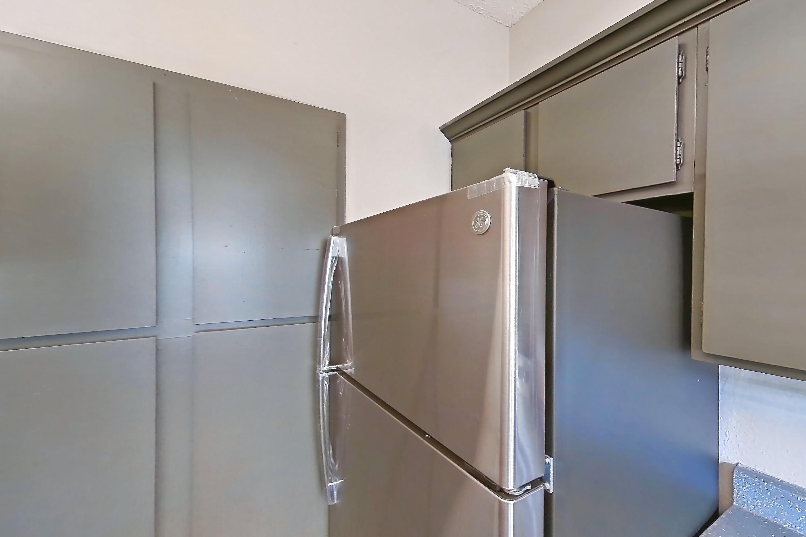 Kitchen with dark countertops, dishwasher, electric range, fireplace, light wood-finish flooring, oven/range, refrigerator, stainless steel appliances, and tile fireplace, Apartment 3013 at Waterford on the Meadow