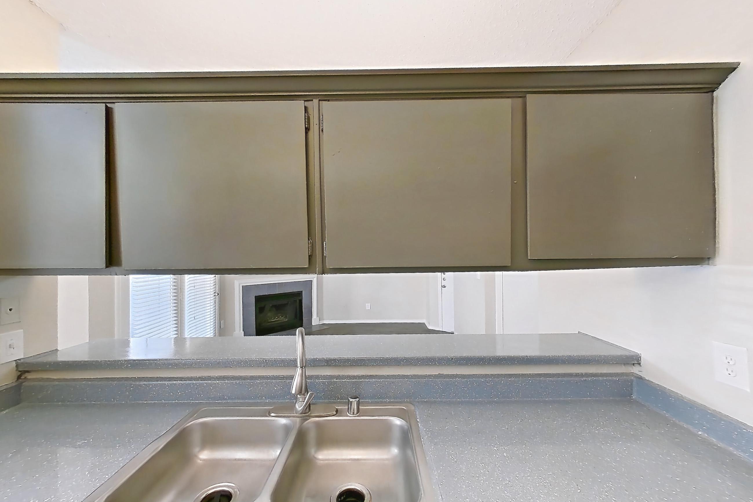 Kitchen with dark countertops, dishwasher, electric range, fireplace, light wood-finish flooring, oven/range, refrigerator, stainless steel appliances, and tile fireplace, Apartment 3013 at Waterford on the Meadow