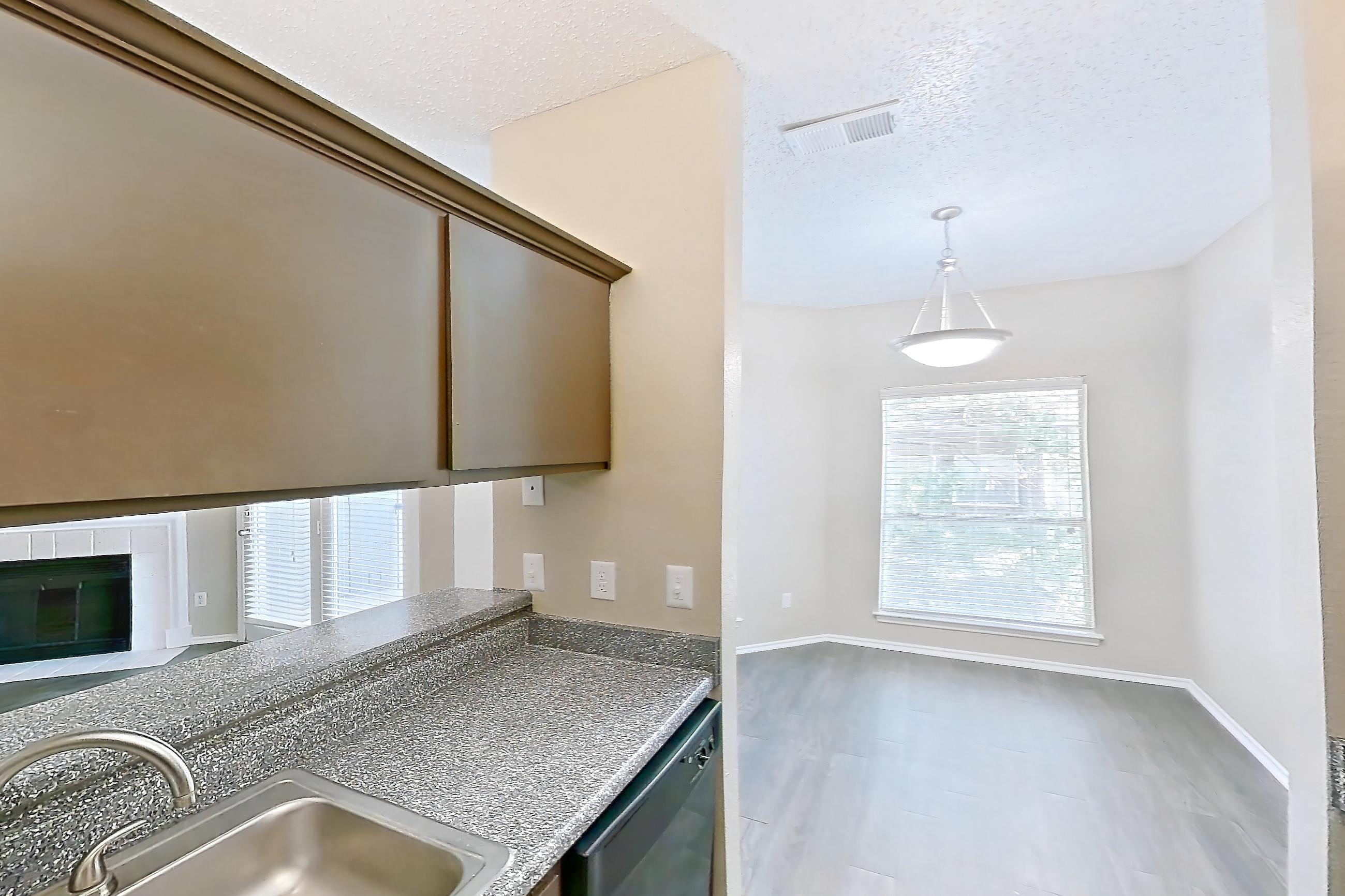 Kitchen with dark countertops, dark stone countertops, dishwasher, electric range, fireplace, light wood-finish flooring, oven/range, stainless steel appliances, and tile fireplace, Apartment 3122 at Waterford on the Meadow