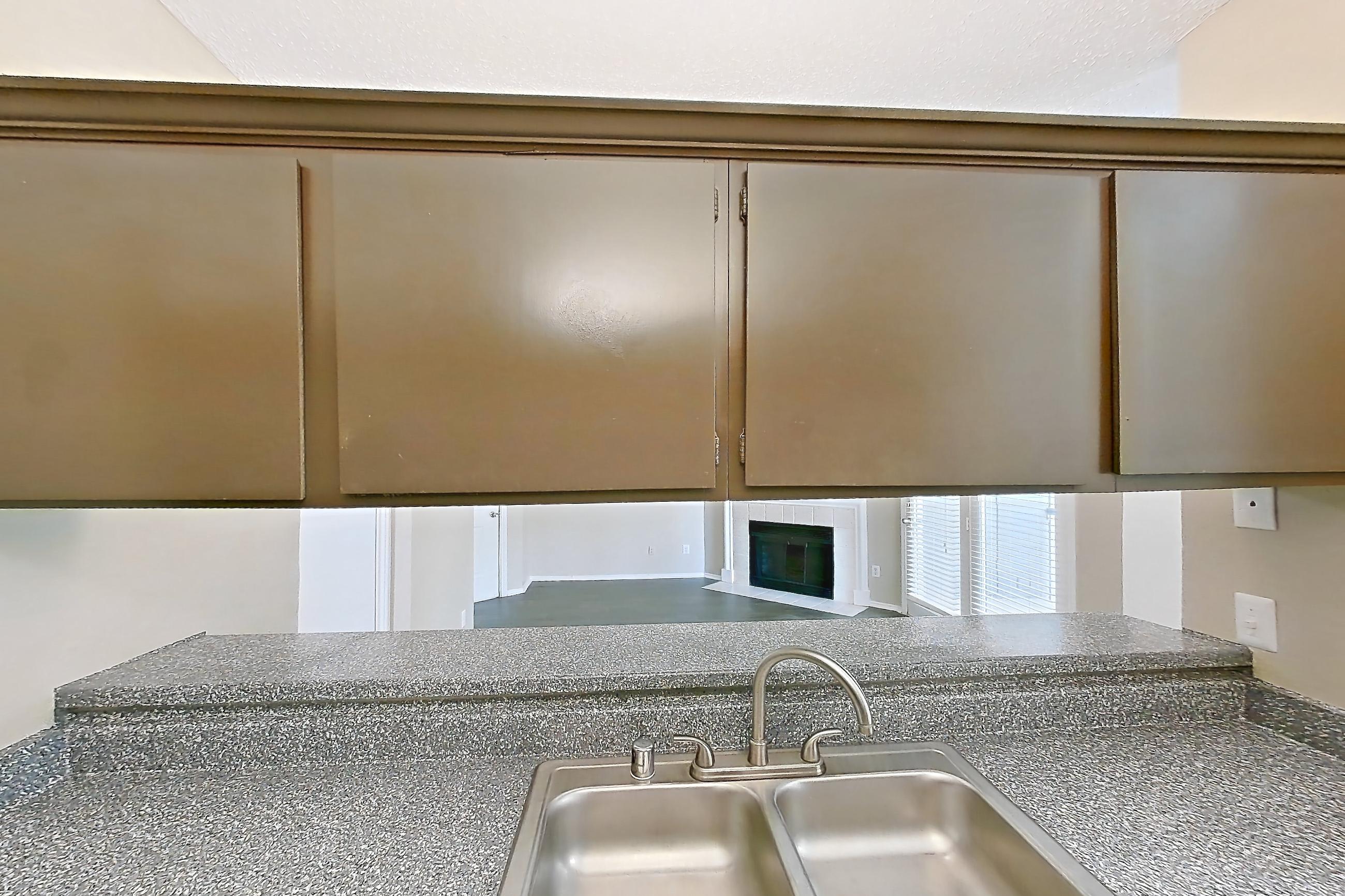 Kitchen with dark countertops, dark stone countertops, dishwasher, electric range, fireplace, light wood-finish flooring, oven/range, stainless steel appliances, and tile fireplace, Apartment 3122 at Waterford on the Meadow