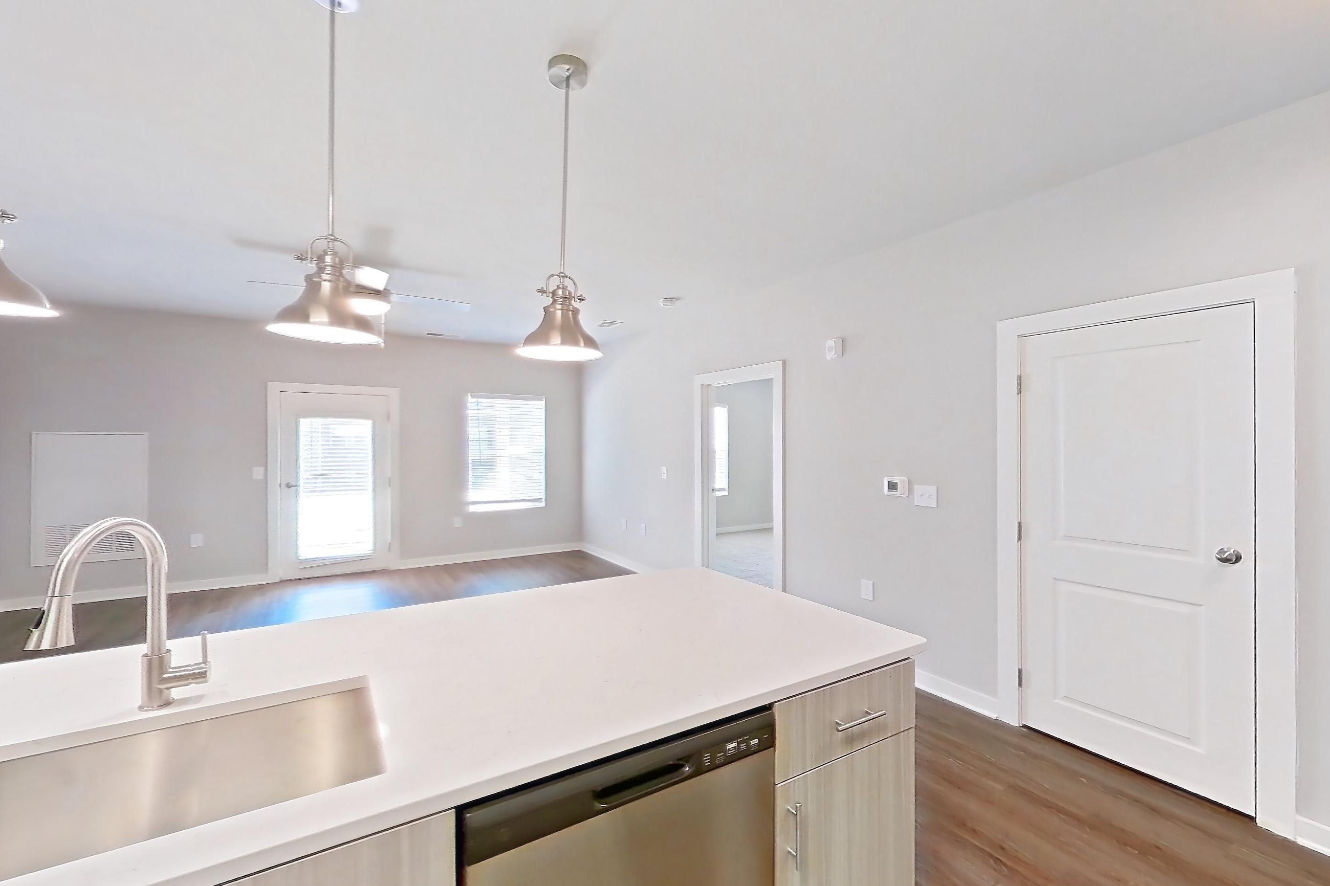 Kitchen with dark wood-finish flooring, dishwasher, electric range, light countertops, light stone countertops, light wood-finish flooring, microwave, oven/range, refrigerator, stainless steel appliances, and water & ice dispenser, Apartment 2-100 at The Soho
