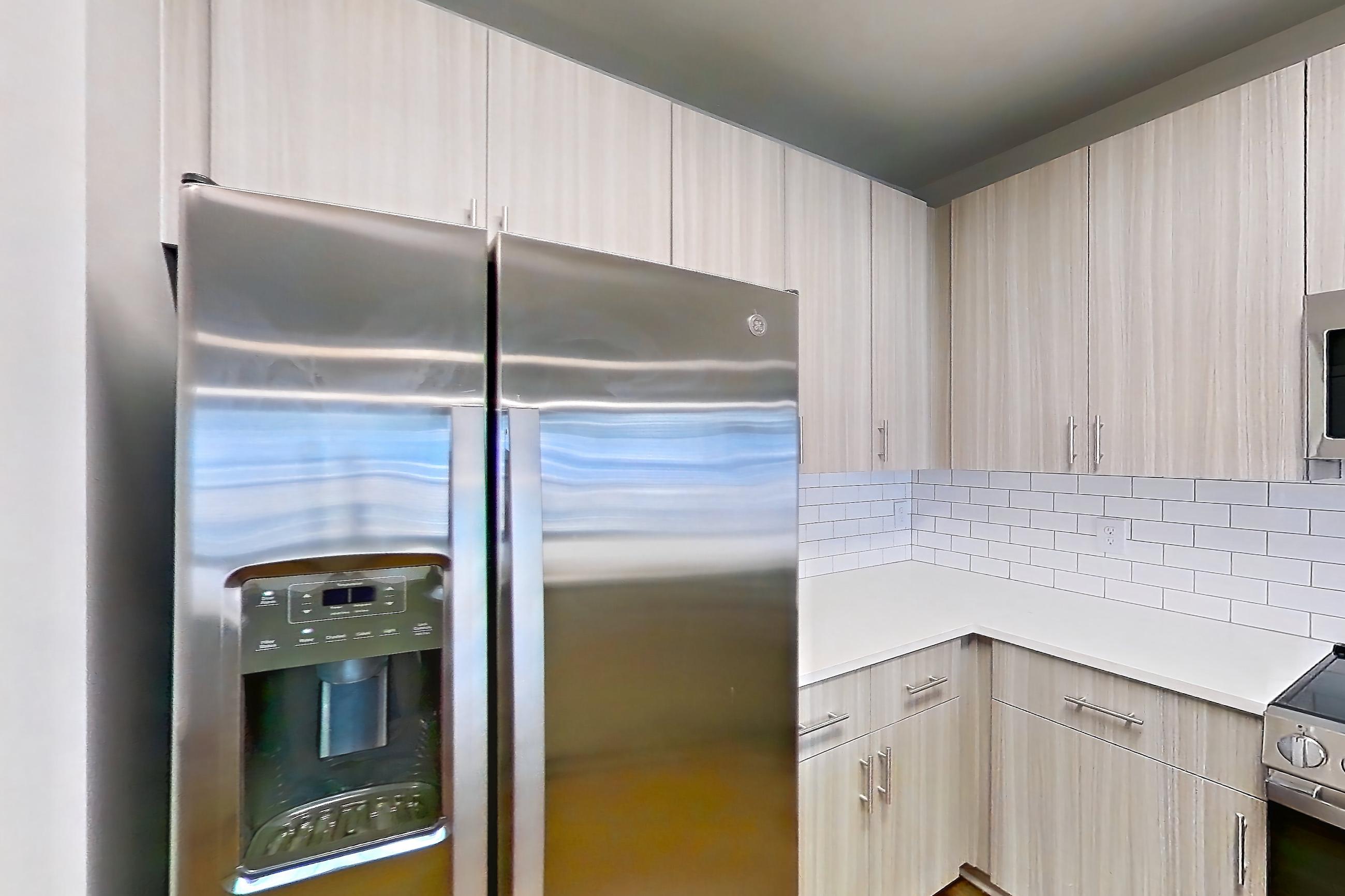 Kitchen with dark wood-finish flooring, dishwasher, electric range, light countertops, light stone countertops, light wood-finish flooring, microwave, oven/range, refrigerator, stainless steel appliances, and water & ice dispenser, Apartment 2-405 at The Soho