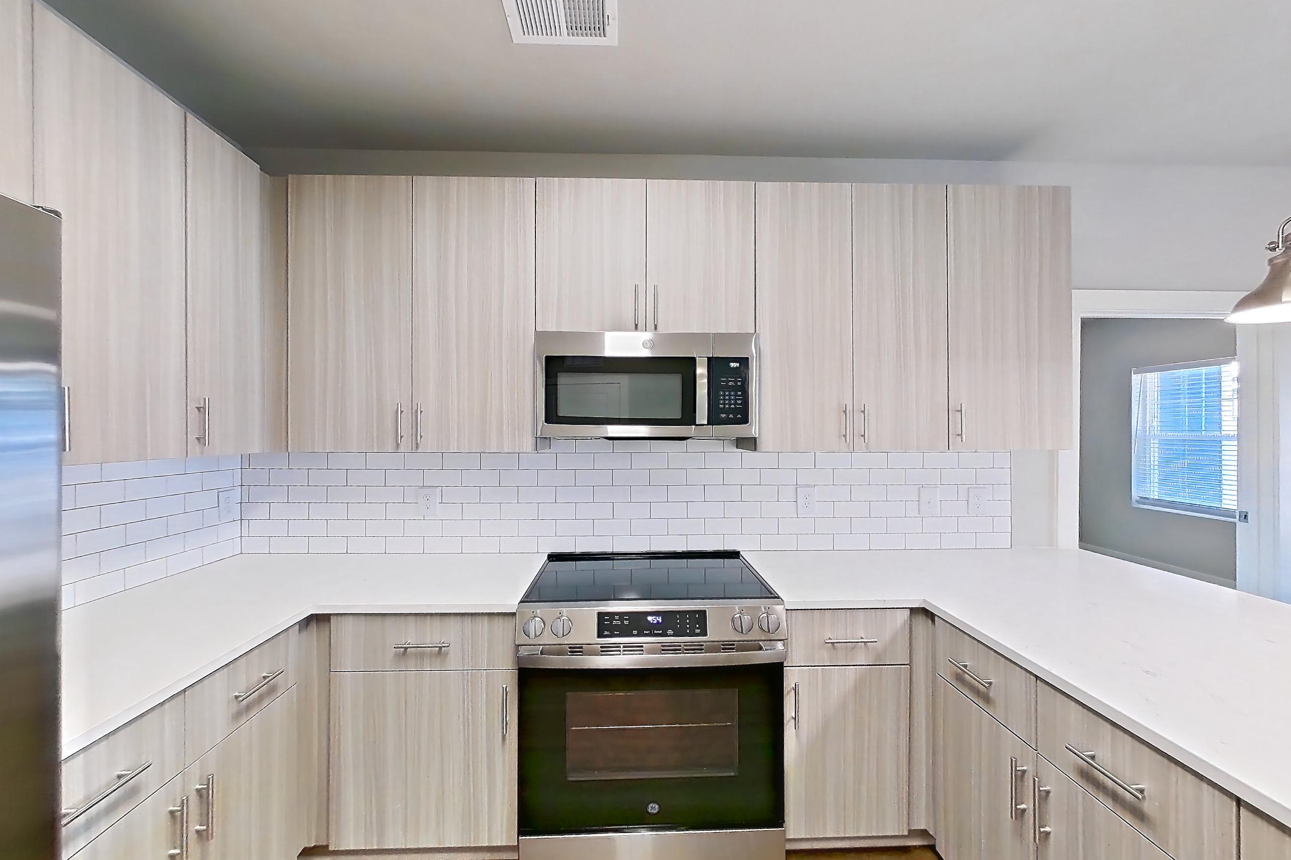 Kitchen with dark wood-finish flooring, dishwasher, electric range, light countertops, light stone countertops, light wood-finish flooring, microwave, oven/range, refrigerator, stainless steel appliances, and water & ice dispenser, Apartment 2-405 at The Soho