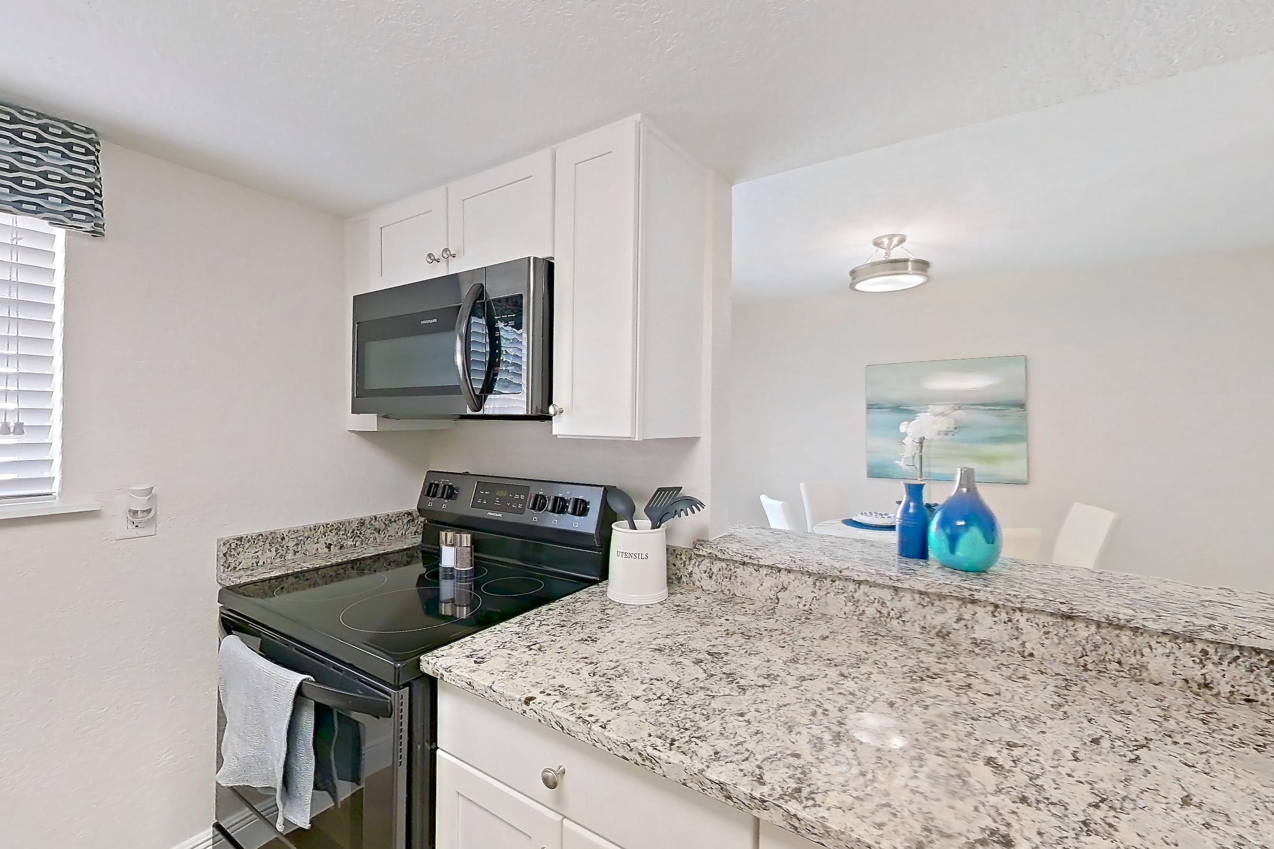 Kitchen with black appliances, dark wood-finish flooring, dishwasher, electric range, light countertops, light stone countertops, light wood-finish flooring, oven/range, and stainless steel appliances, Apartment A4 at Cypress West