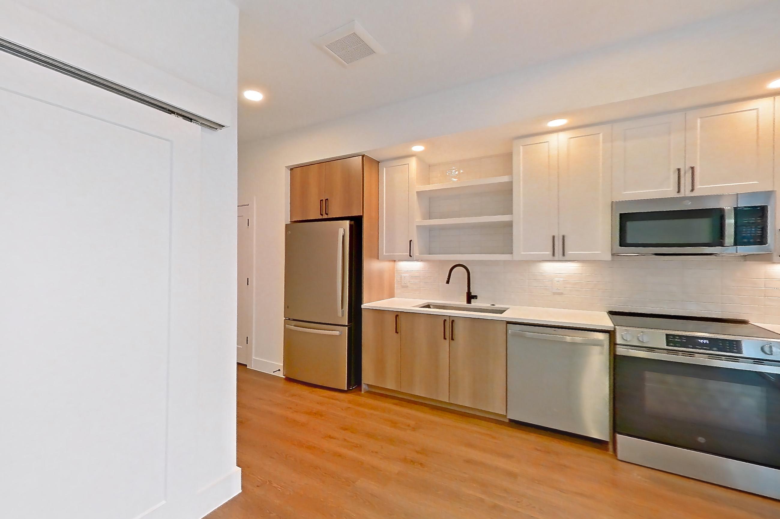 Living space with dishwasher, electric range, light countertops, light stone countertops, light wood-finish flooring, microwave, oven/range, refrigerator, and stainless steel appliances, Apartment 405 at The Watson