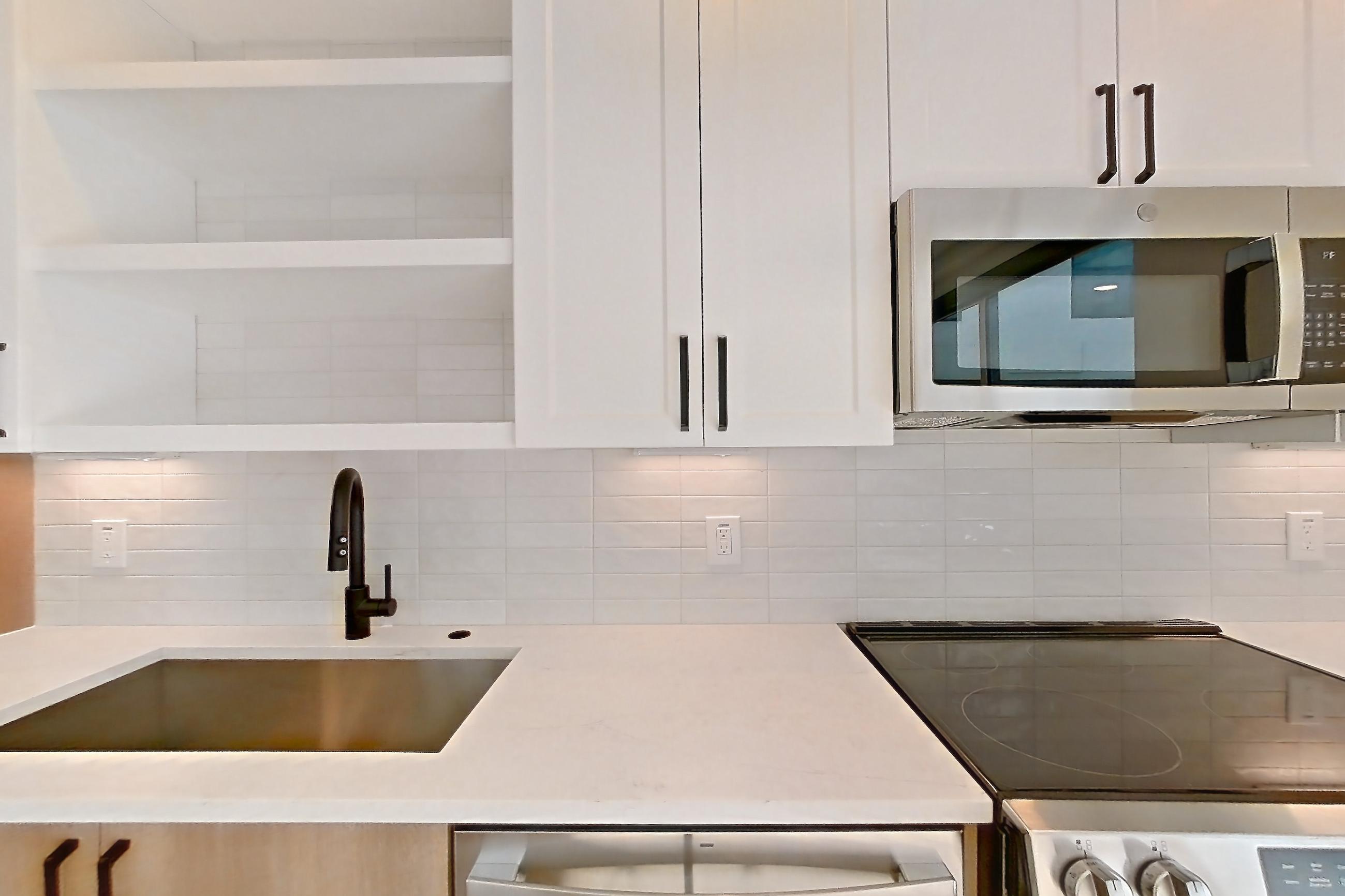 Kitchen with dishwasher, electric range, light countertops, light stone countertops, light wood-finish flooring, microwave, oven/range, refrigerator, and stainless steel appliances, Apartment 505 at The Watson