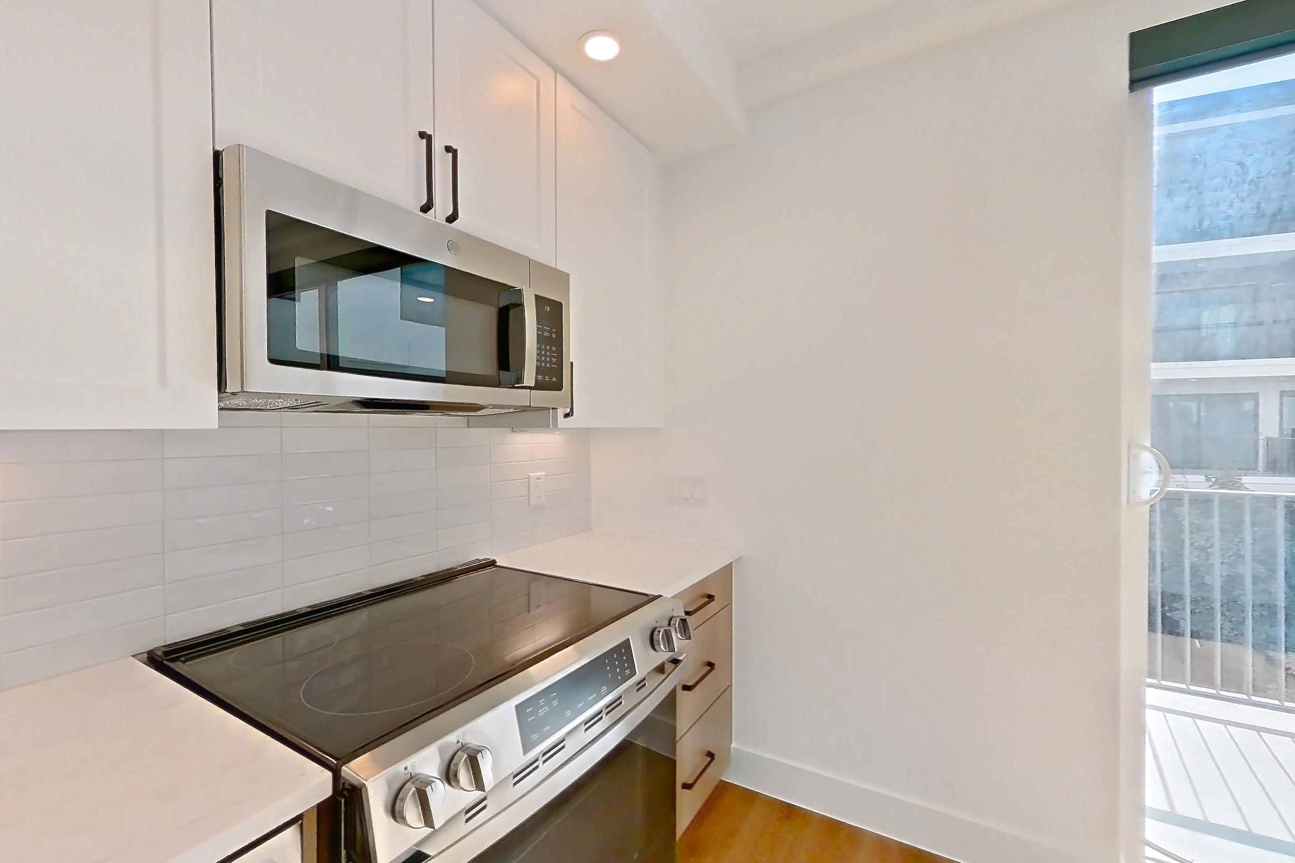 Kitchen with dishwasher, electric range, light countertops, light stone countertops, light wood-finish flooring, microwave, oven/range, refrigerator, and stainless steel appliances, Apartment 505 at The Watson