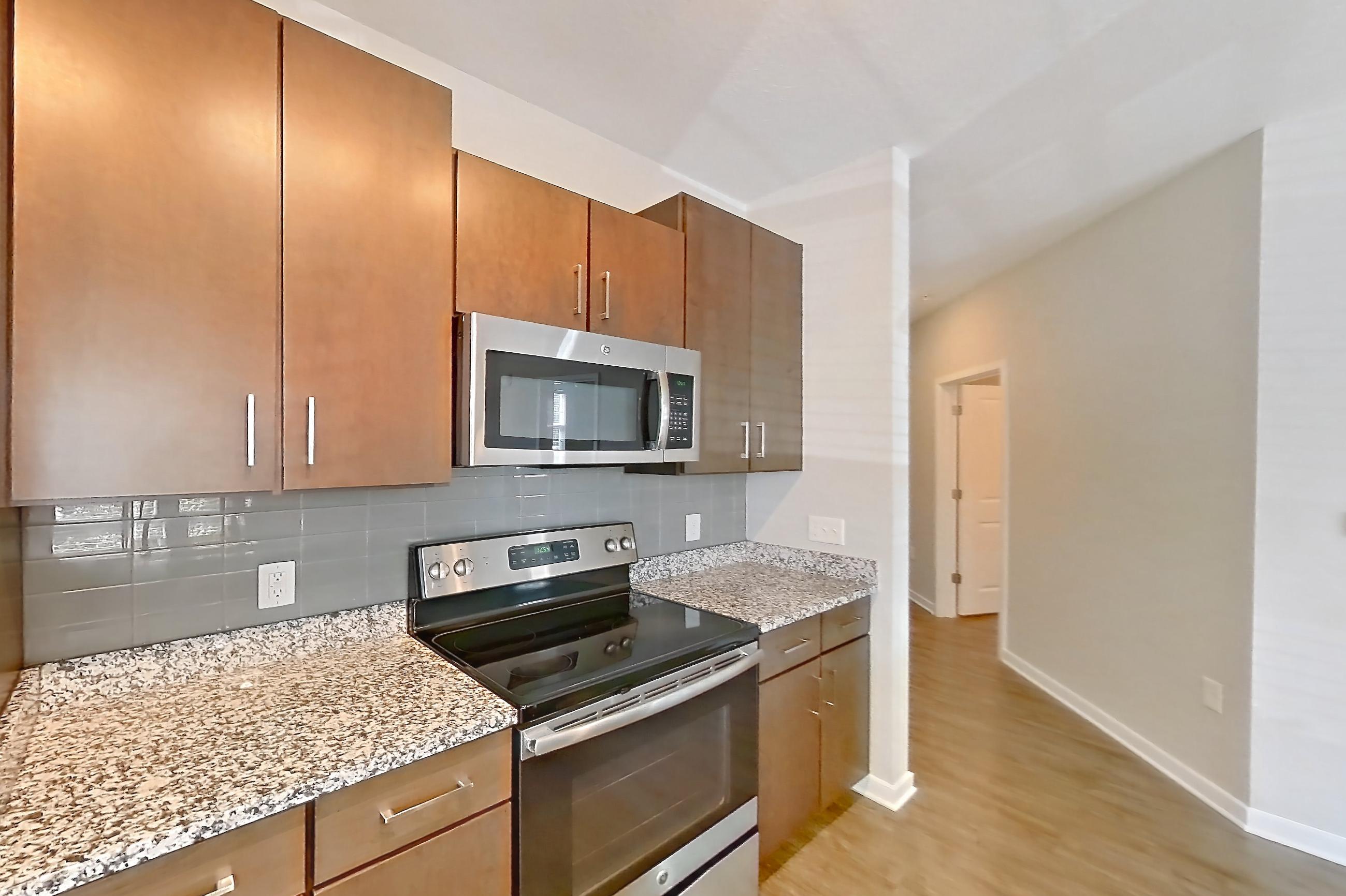 Kitchen with dishwasher, electric range, kitchen island, light countertops, light stone countertops, light wood-finish flooring, oven/range, and stainless steel appliances, Apartment 101 at Lake Nona Ariel Apartments