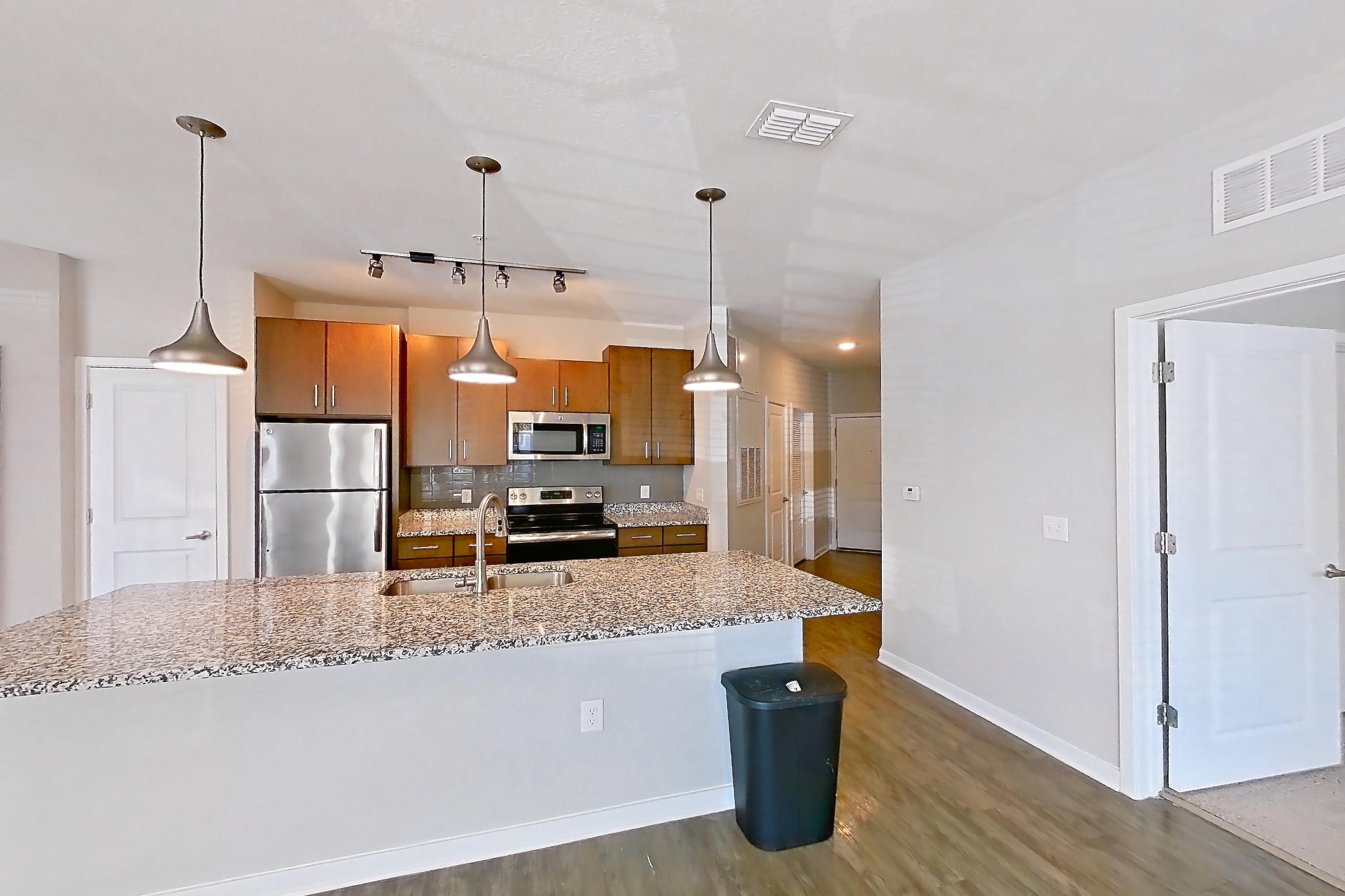 Living room with dark wood-finish flooring, electric range, kitchen island, light countertops, light stone countertops, oven/range, refrigerator, and stainless steel appliances, Apartment 101 at Lake Nona Ariel Apartments