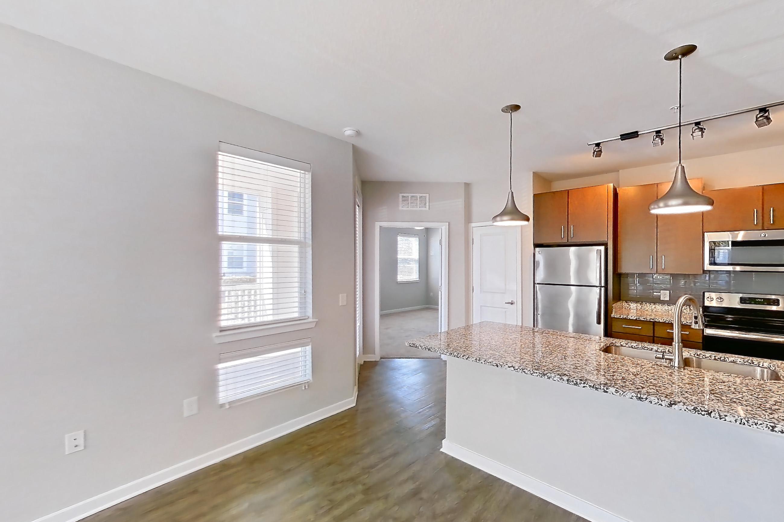 Living room with dark wood-finish flooring, electric range, kitchen island, light countertops, light stone countertops, oven/range, refrigerator, and stainless steel appliances, Apartment 101 at Lake Nona Ariel Apartments