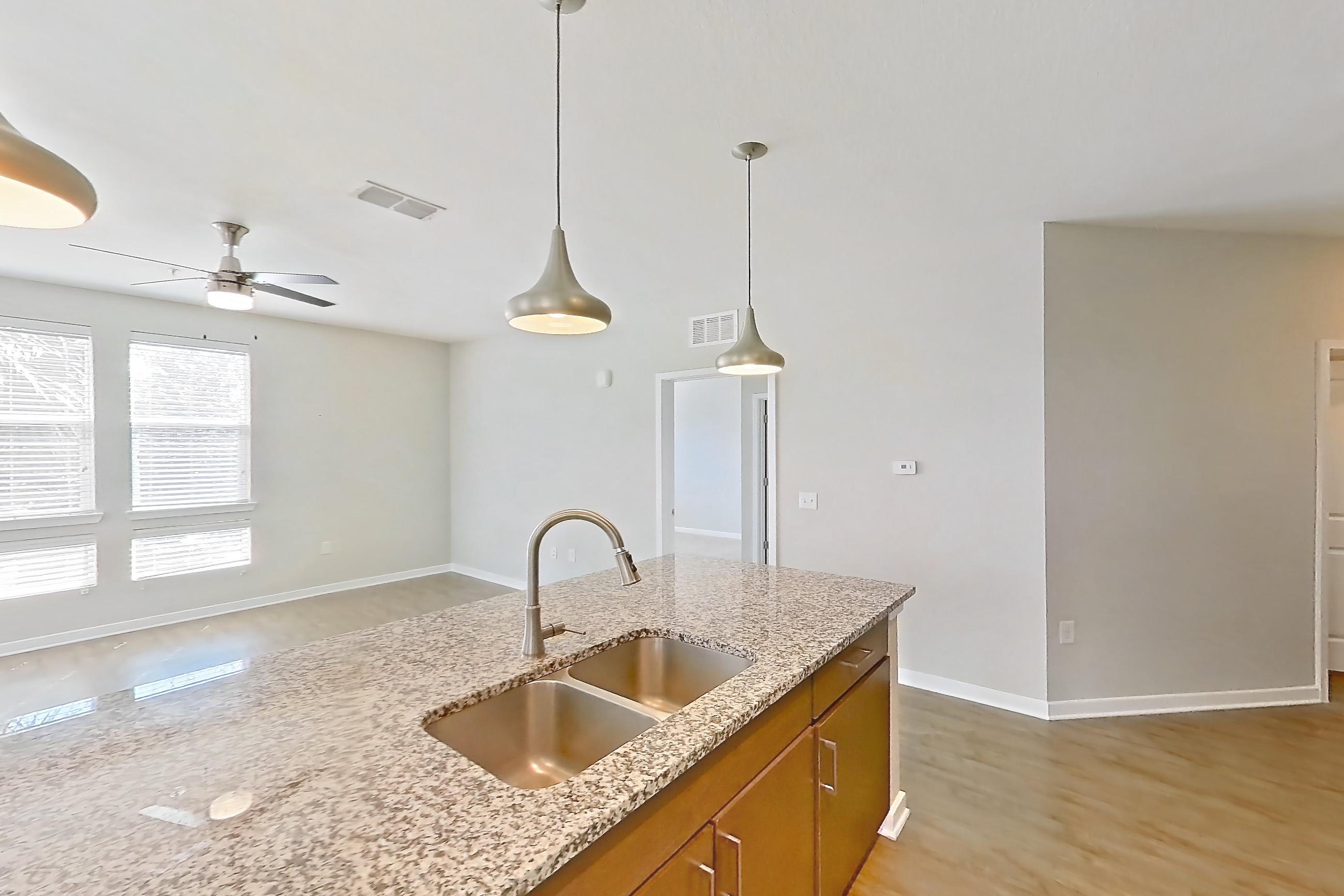 Kitchen with dishwasher, kitchen island, light stone countertops, light wood-finish flooring, refrigerator, and stainless steel appliances, Apartment 208 at Lake Nona Ariel Apartments