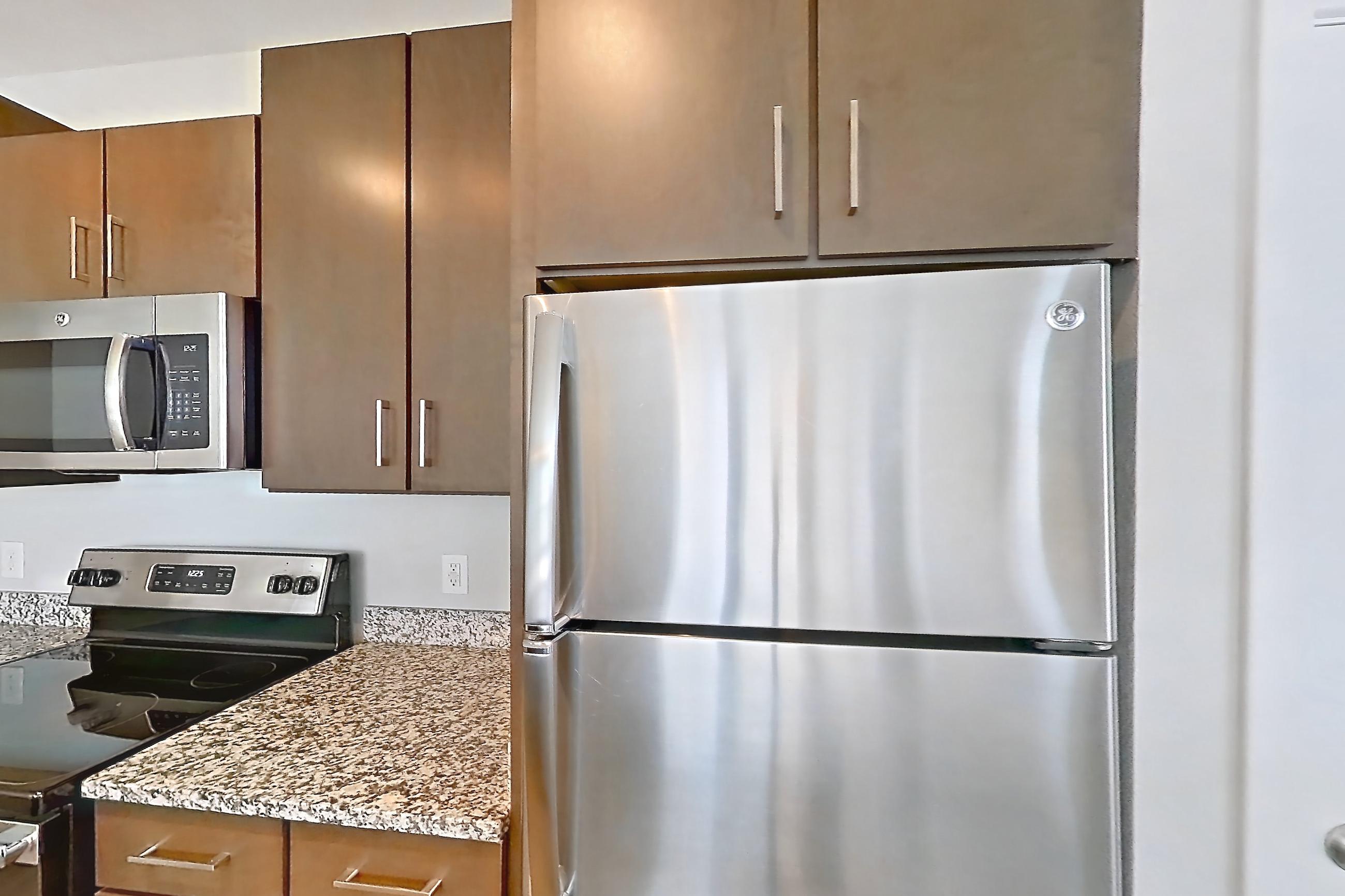 Kitchen with dishwasher, kitchen island, light stone countertops, light wood-finish flooring, refrigerator, and stainless steel appliances, Apartment 208 at Lake Nona Ariel Apartments