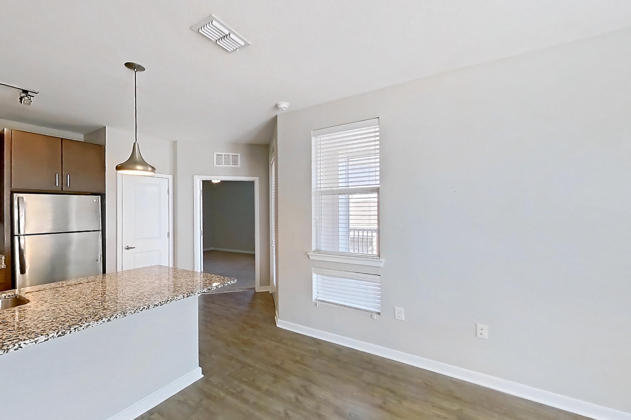 Living room with dark wood-finish flooring, electric range, kitchen island, light countertops, light stone countertops, oven/range, refrigerator, and stainless steel appliances, Apartment 208 at Lake Nona Ariel Apartments