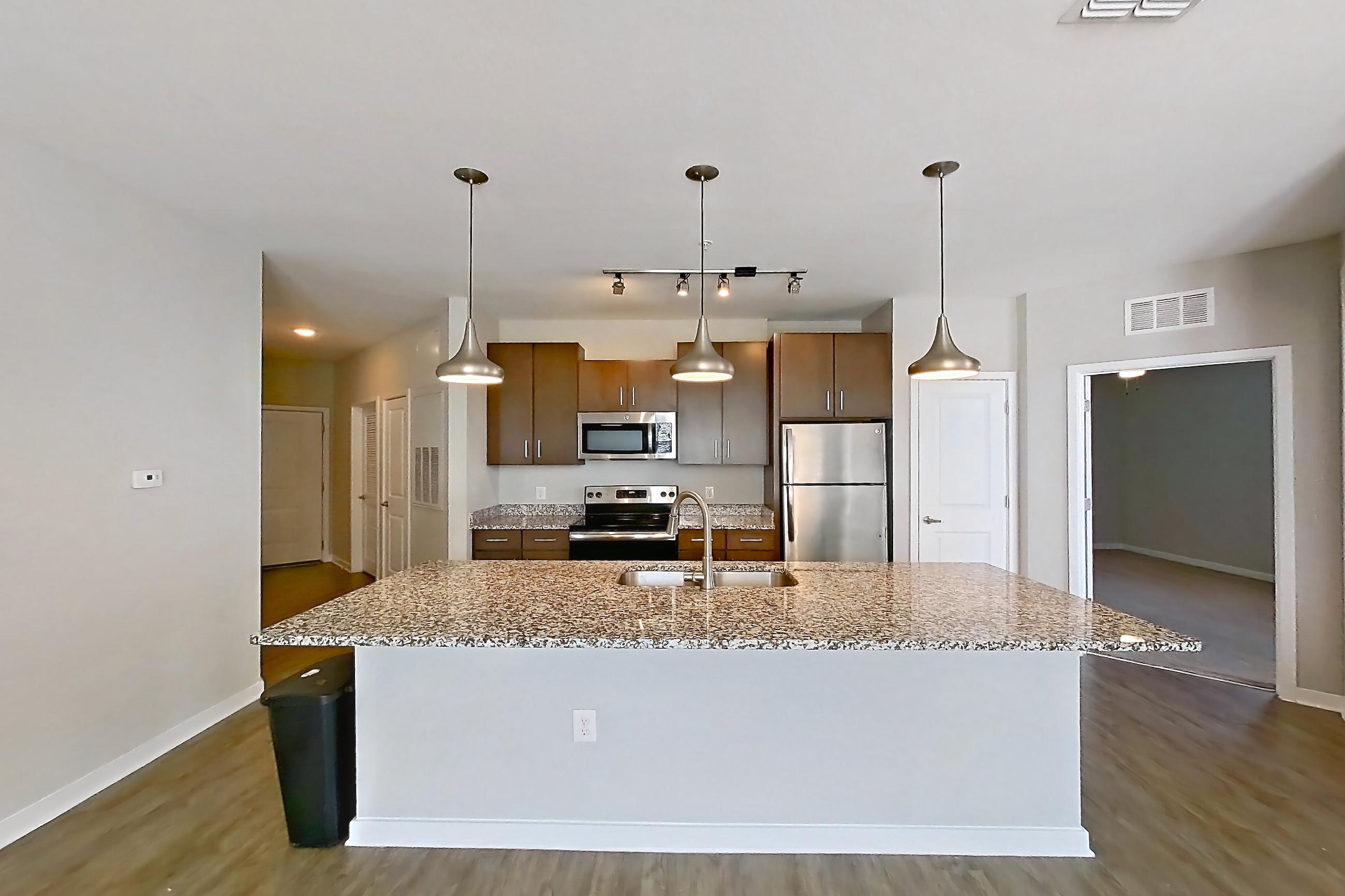 Living room with dark wood-finish flooring, electric range, kitchen island, light countertops, light stone countertops, oven/range, refrigerator, and stainless steel appliances, Apartment 208 at Lake Nona Ariel Apartments