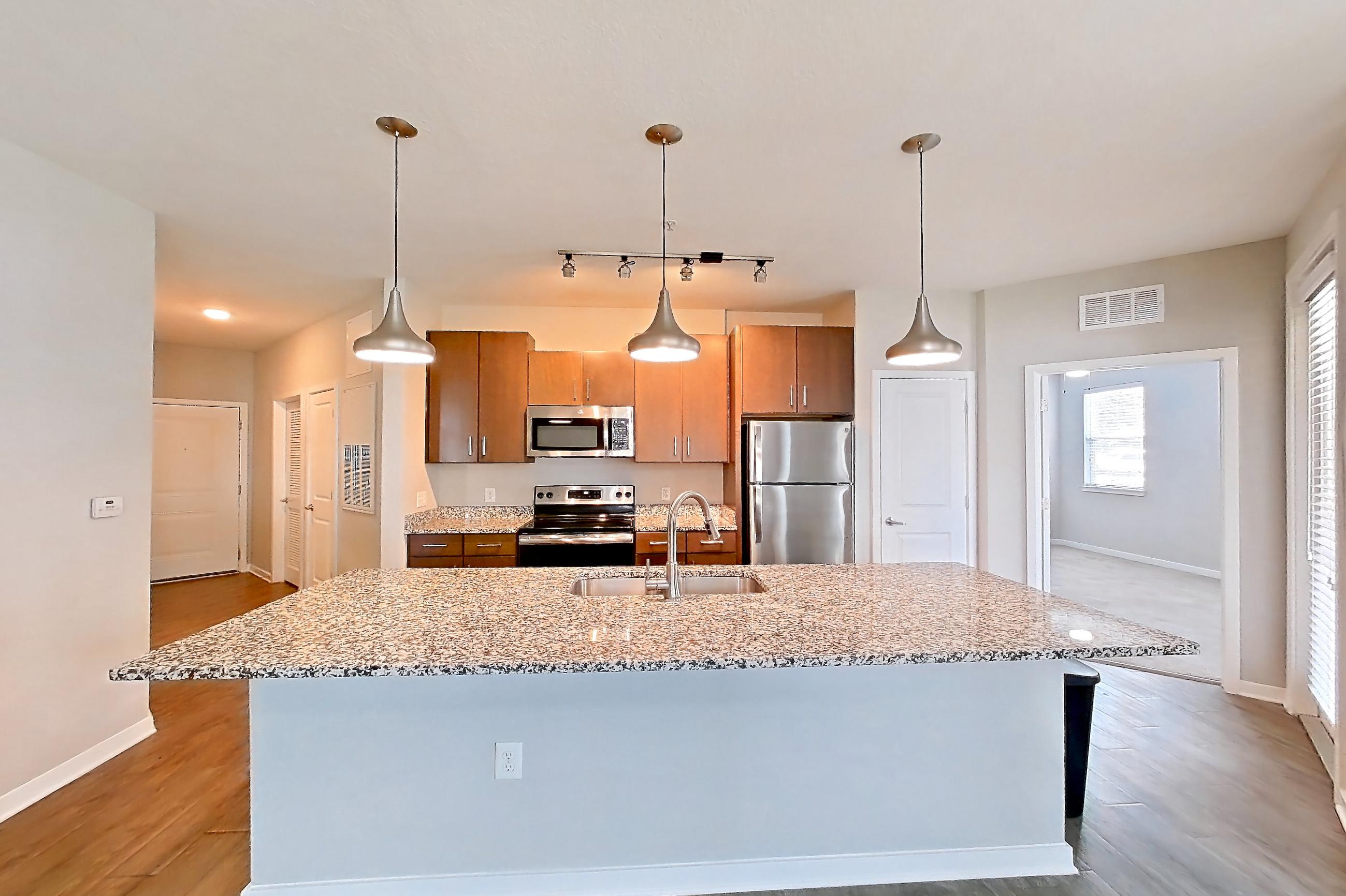 Living room with dark wood-finish flooring, electric range, kitchen island, light countertops, light stone countertops, light wood-finish flooring, microwave, oven/range, refrigerator, and stainless steel appliances, Apartment 103 at Lake Nona Ariel Apartments