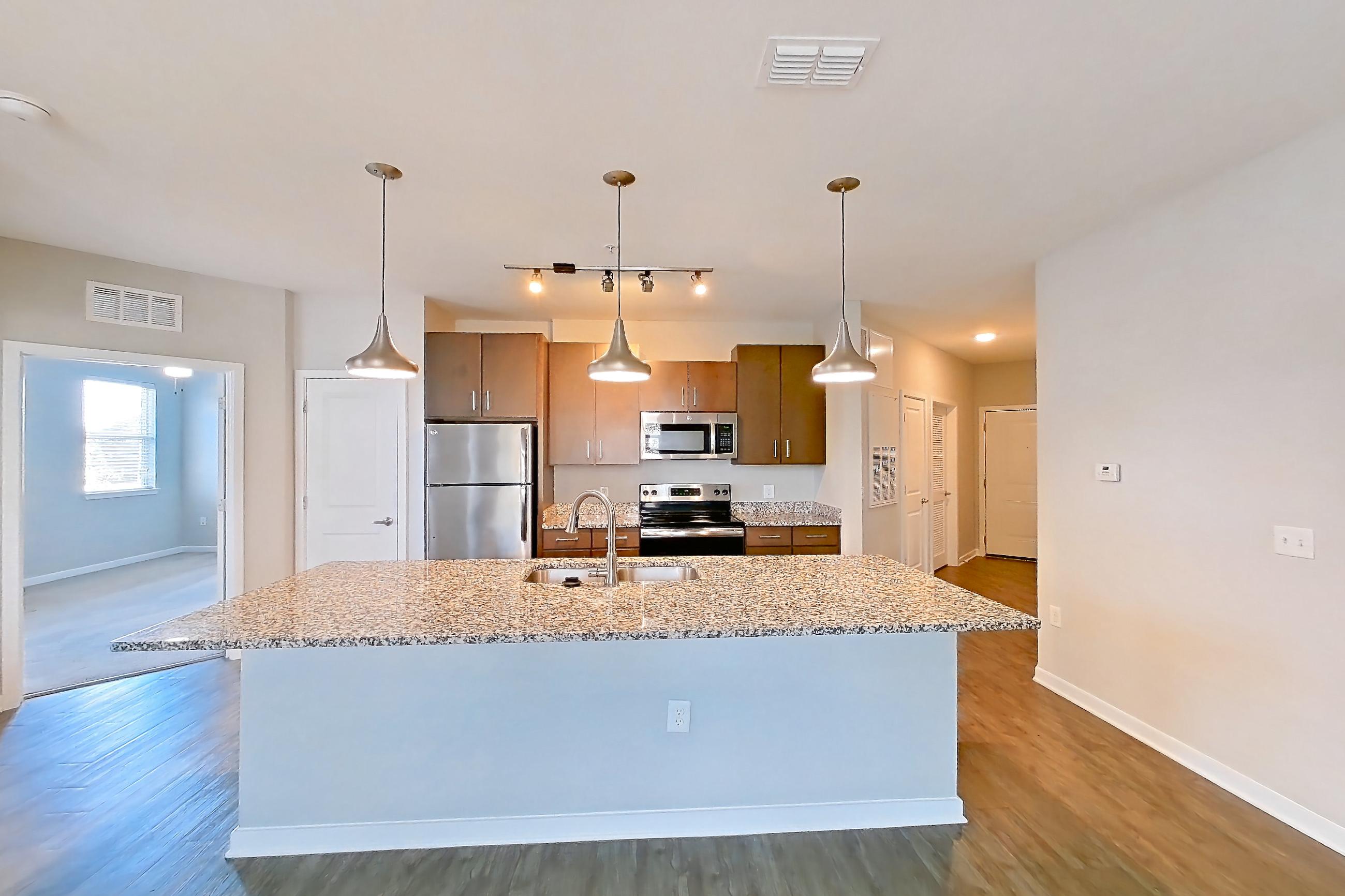Living room with dark wood-finish flooring, electric range, kitchen island, light countertops, light stone countertops, oven/range, refrigerator, and stainless steel appliances, Apartment 208 at Lake Nona Ariel Apartments