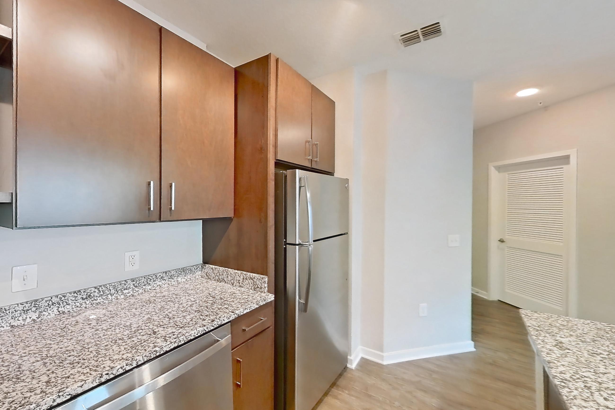Kitchen with dishwasher, electric range, light countertops, light stone countertops, light wood-finish flooring, microwave, oven/range, refrigerator, and stainless steel appliances, Apartment 208 at Lake Nona Ariel Apartments