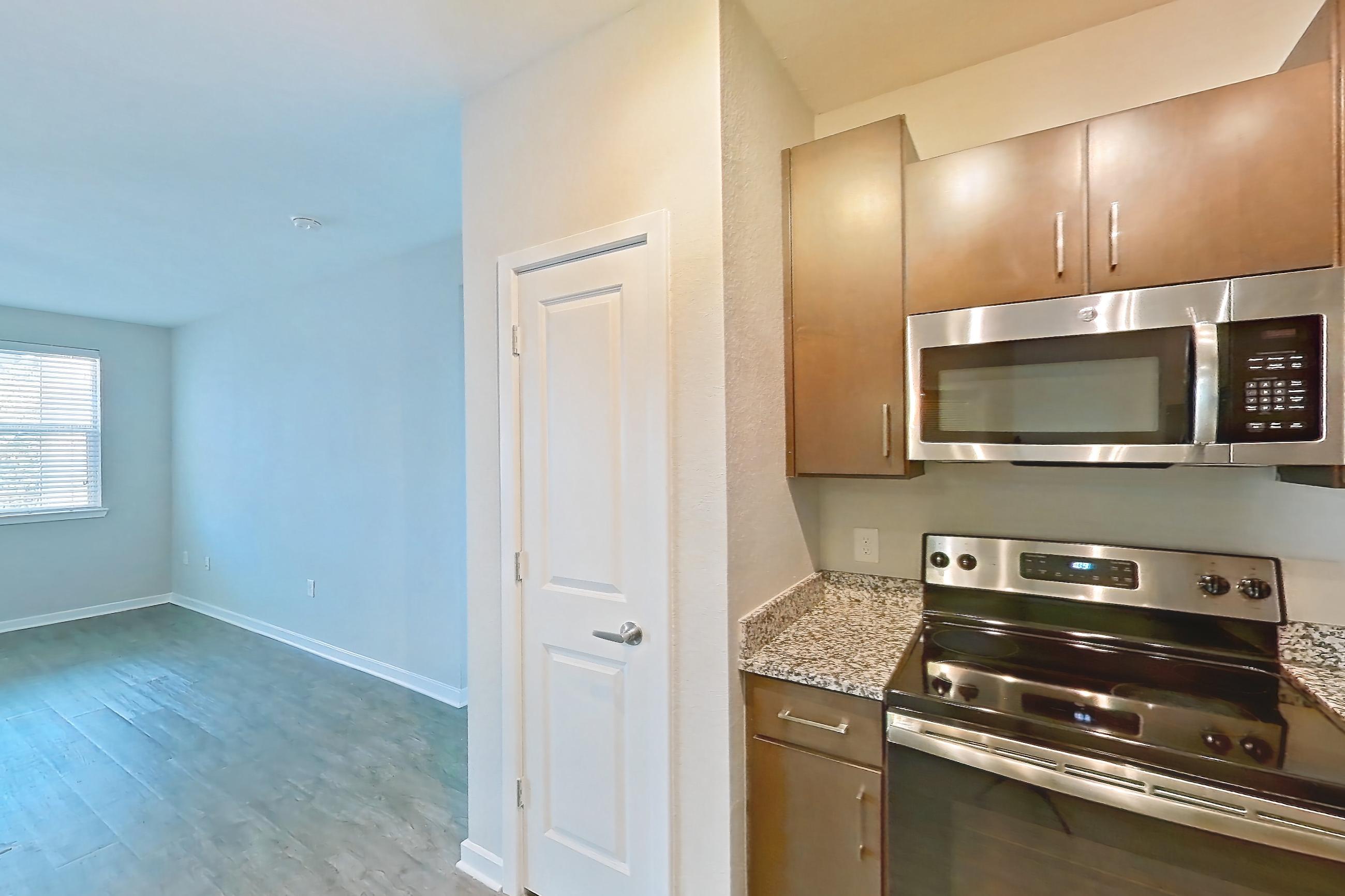 Kitchen with dishwasher, electric range, light countertops, light stone countertops, light wood-finish flooring, microwave, oven/range, refrigerator, and stainless steel appliances, Apartment 208 at Lake Nona Ariel Apartments