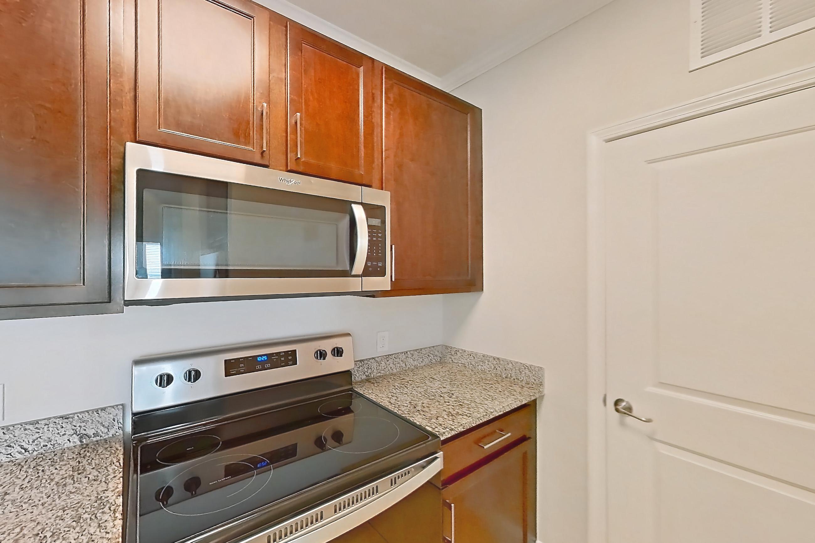 Kitchen with dishwasher, electric range, light carpet, light countertops, light stone countertops, light tile flooring, microwave, oven/range, refrigerator, and stainless steel appliances, Apartment 0132 at Lake Nona Water Mark