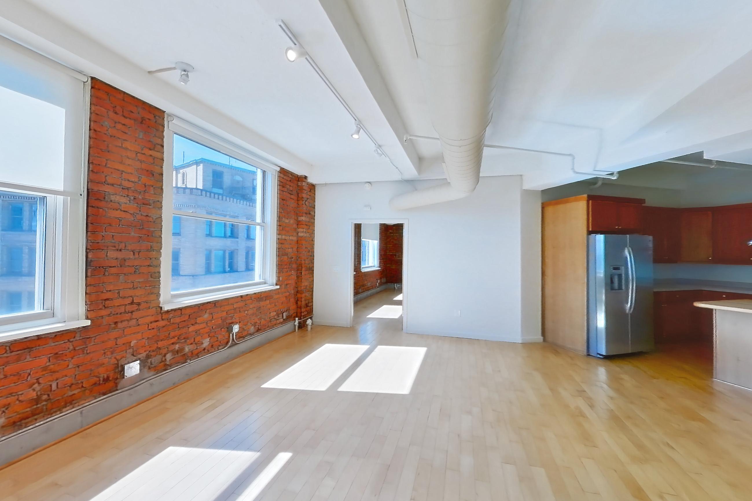 Living space with dishwasher, light countertops, light wood-finish flooring, refrigerator, stainless steel appliances, water & ice dispenser, and wood-finish flooring, Apartment 1301 at Temple Building
