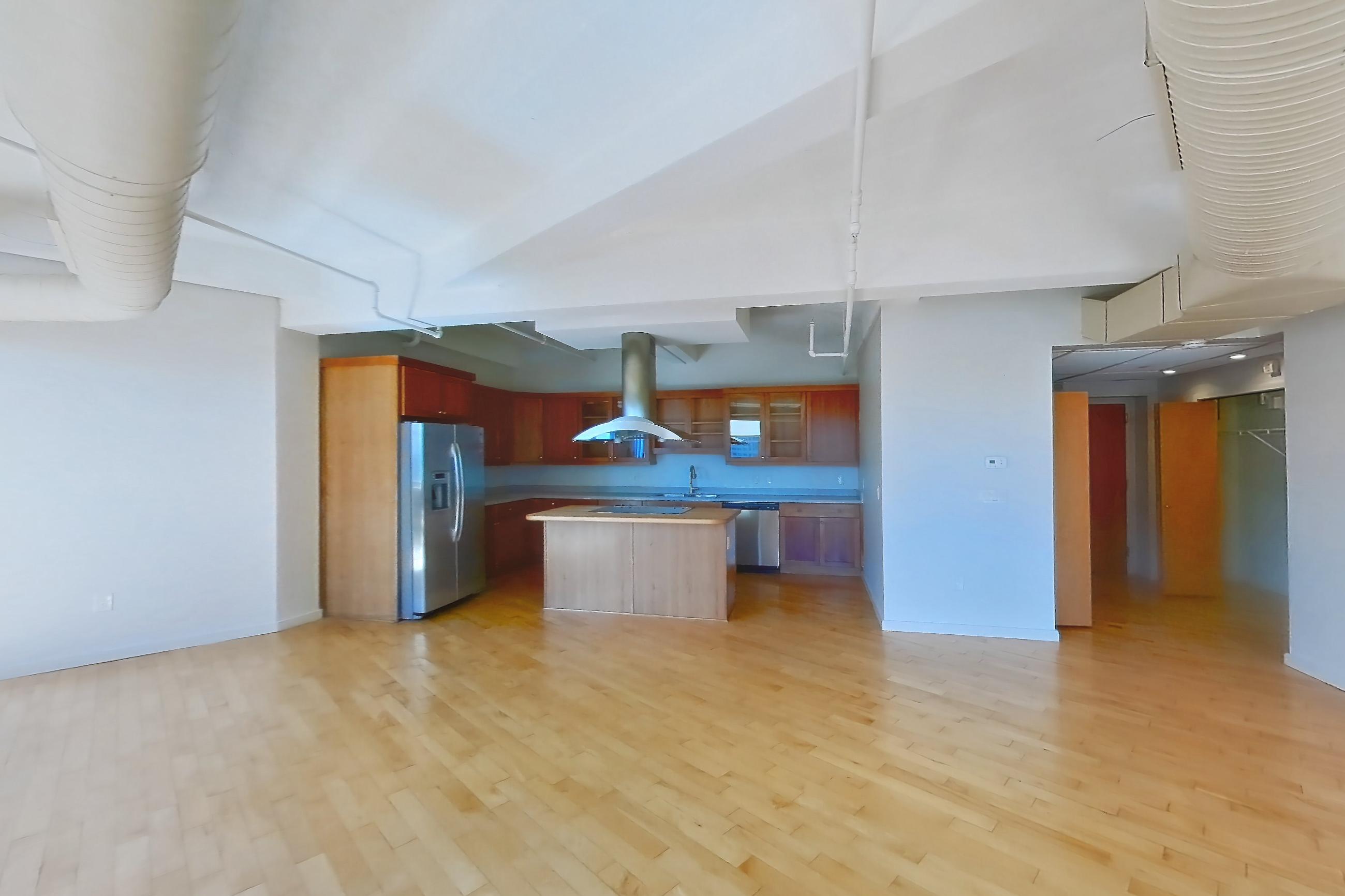 Living space with dishwasher, light countertops, light wood-finish flooring, refrigerator, stainless steel appliances, water & ice dispenser, and wood-finish flooring, Apartment 1301 at Temple Building