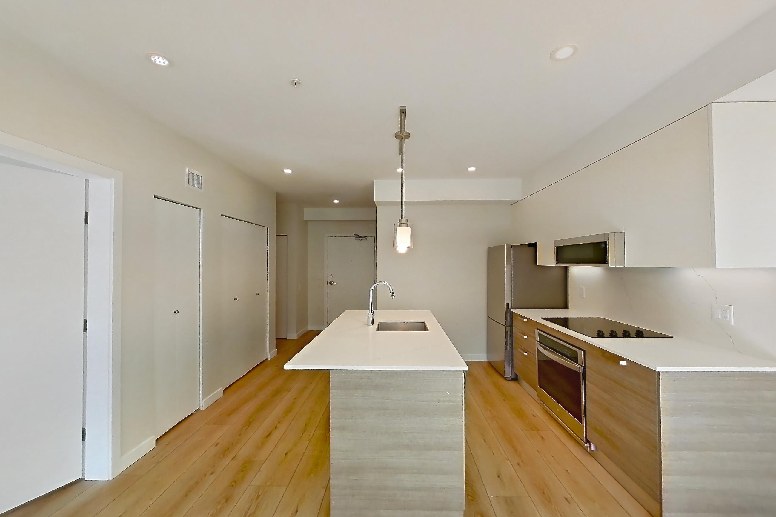 Living room with black appliances, cooktop, electric cooktop, kitchen island, light stone countertops, light wood-finish flooring, oven/range, refrigerator, and stainless steel appliances, Apartment A-204 at Hendry Place