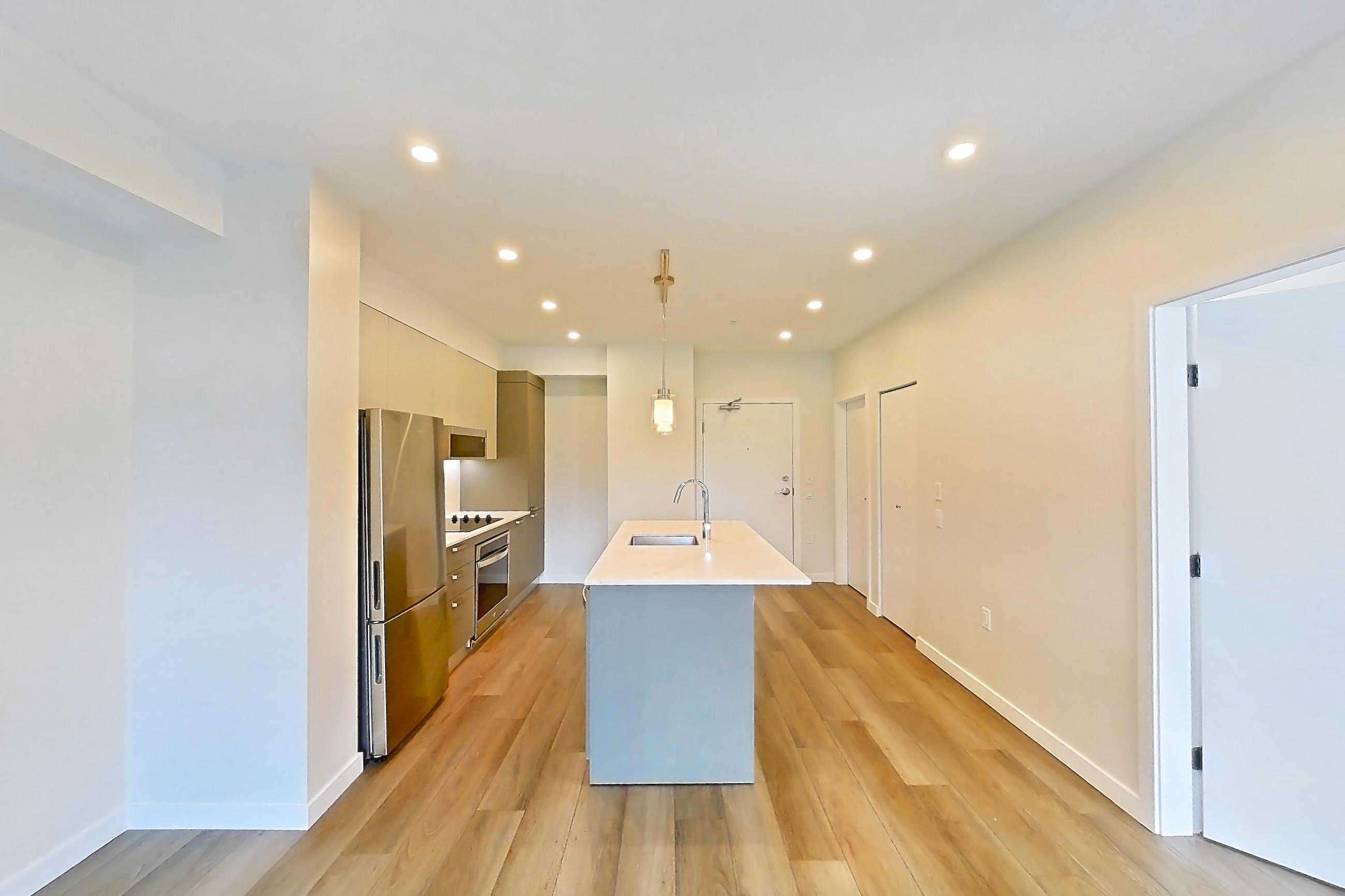 Living room with black appliances, cooktop, electric cooktop, kitchen island, light countertops, light wood-finish flooring, oven/range, refrigerator, and stainless steel appliances, Apartment A-205 at Hendry Place