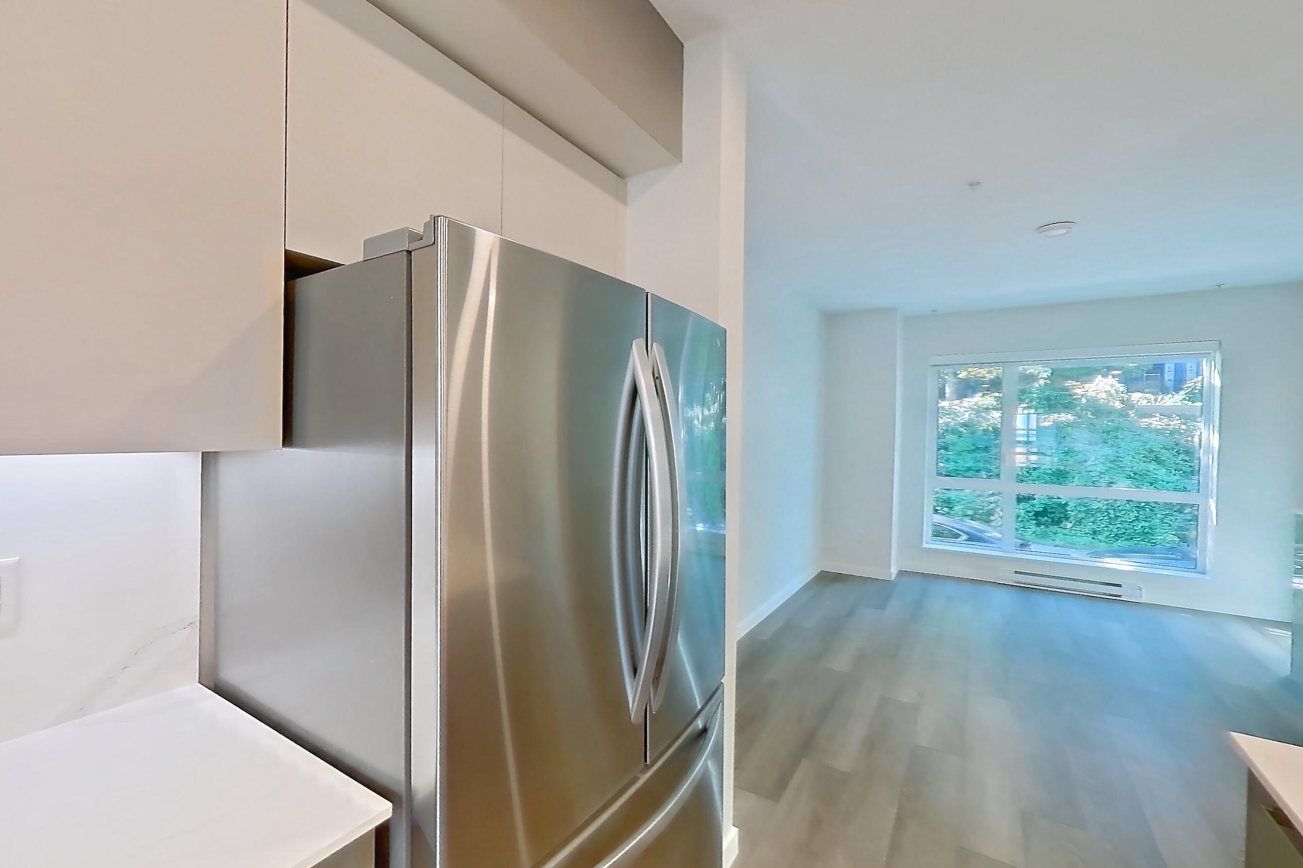 Kitchen with baseboard heating, black appliances, cooktop, dishwasher, electric cooktop, light countertops, light stone countertops, light wood-finish flooring, oven/range, refrigerator, and stainless steel appliances, Apartment T-074 at Hendry Place