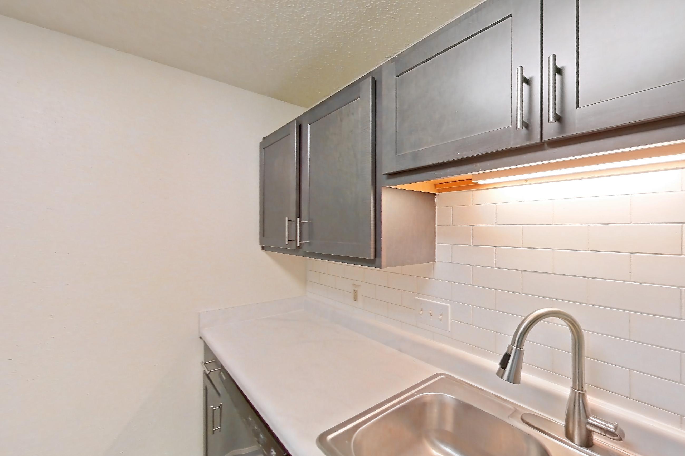 Kitchen with black appliances, dark wood-finish flooring, dishwasher, electric range, light countertops, light wood-finish flooring, microwave, oven/range, refrigerator, and stainless steel appliances, Apartment 64 at Woodwinds