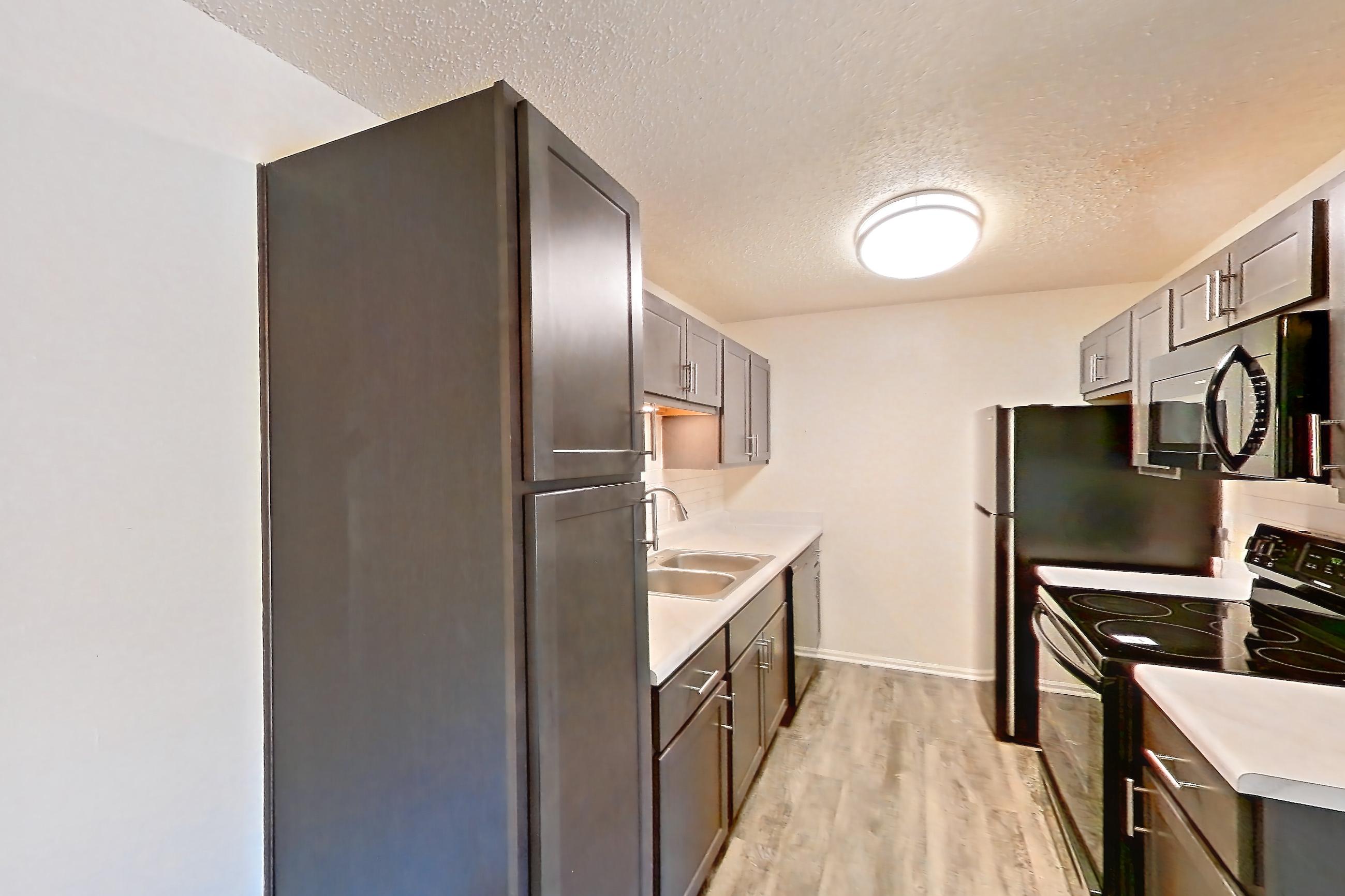 Dining room with black appliances, dark wood-finish flooring, electric range, light countertops, light wood-finish flooring, oven/range, refrigerator, and stainless steel appliances, Apartment 135 at Woodwinds