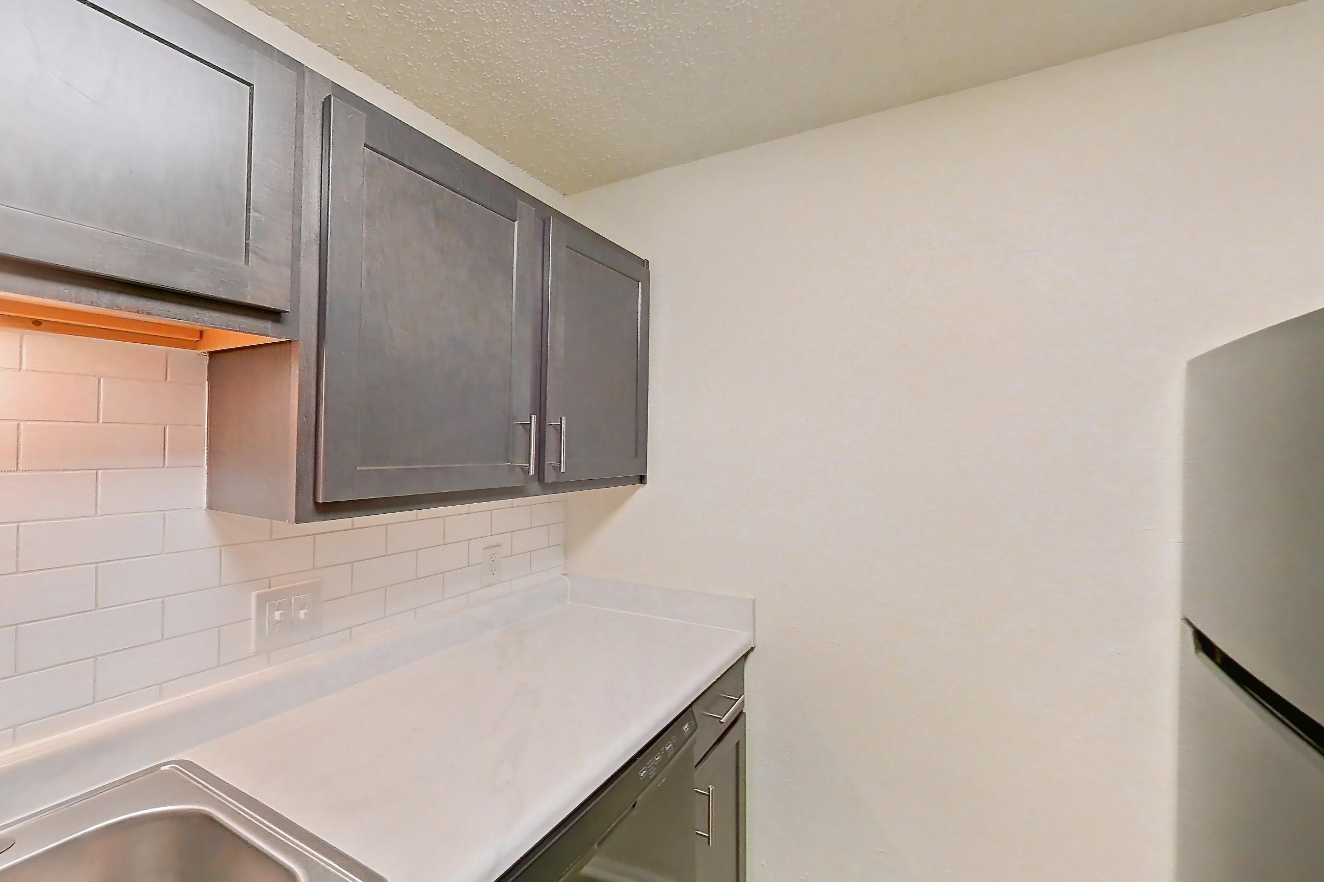 Kitchen with black appliances, dishwasher, electric range, light countertops, light wood-finish flooring, oven/range, refrigerator, and stainless steel appliances, Apartment 135 at Woodwinds