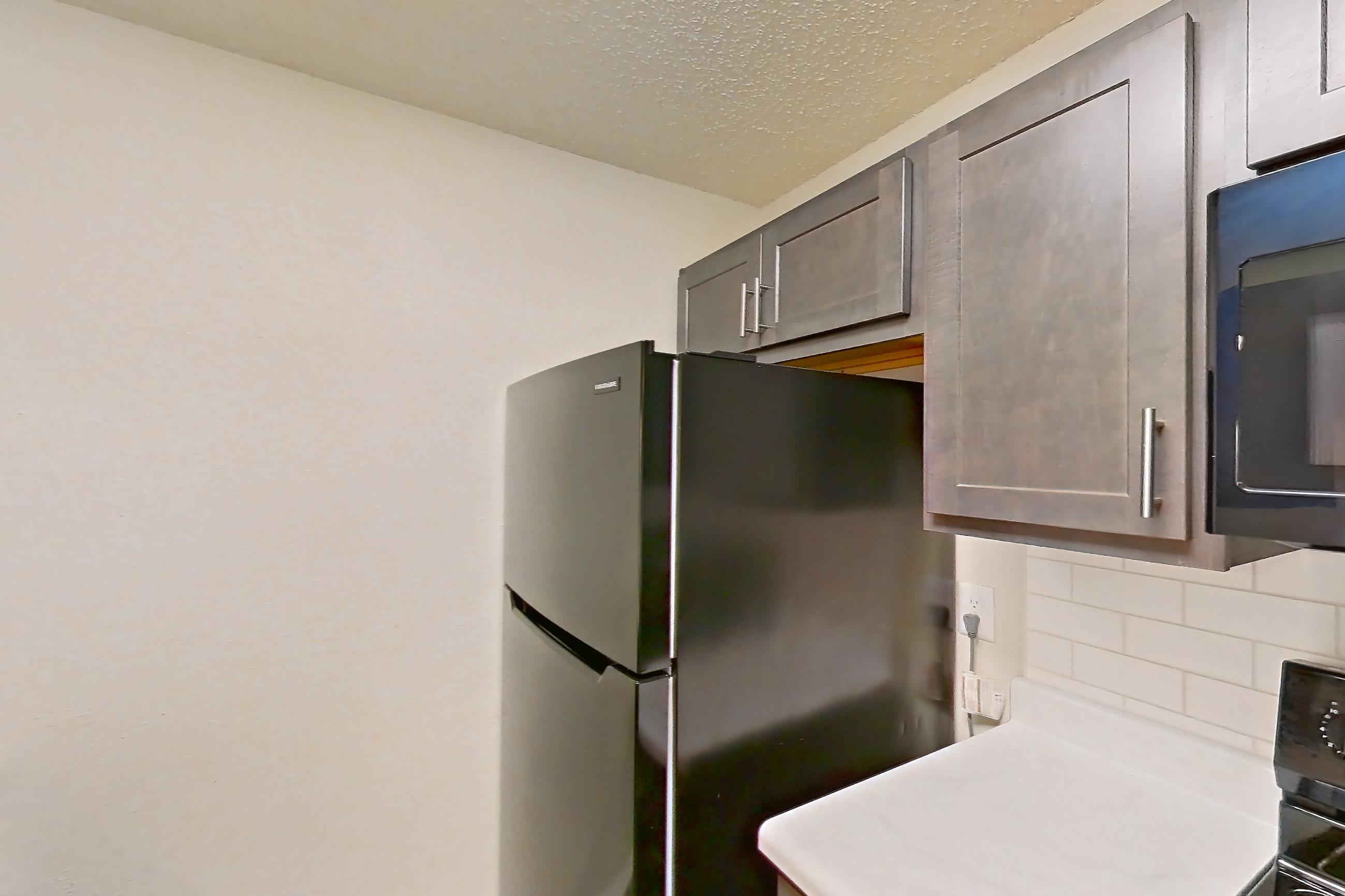 Kitchen with black appliances, dishwasher, electric range, light countertops, light wood-finish flooring, oven/range, refrigerator, and stainless steel appliances, Apartment 135 at Woodwinds