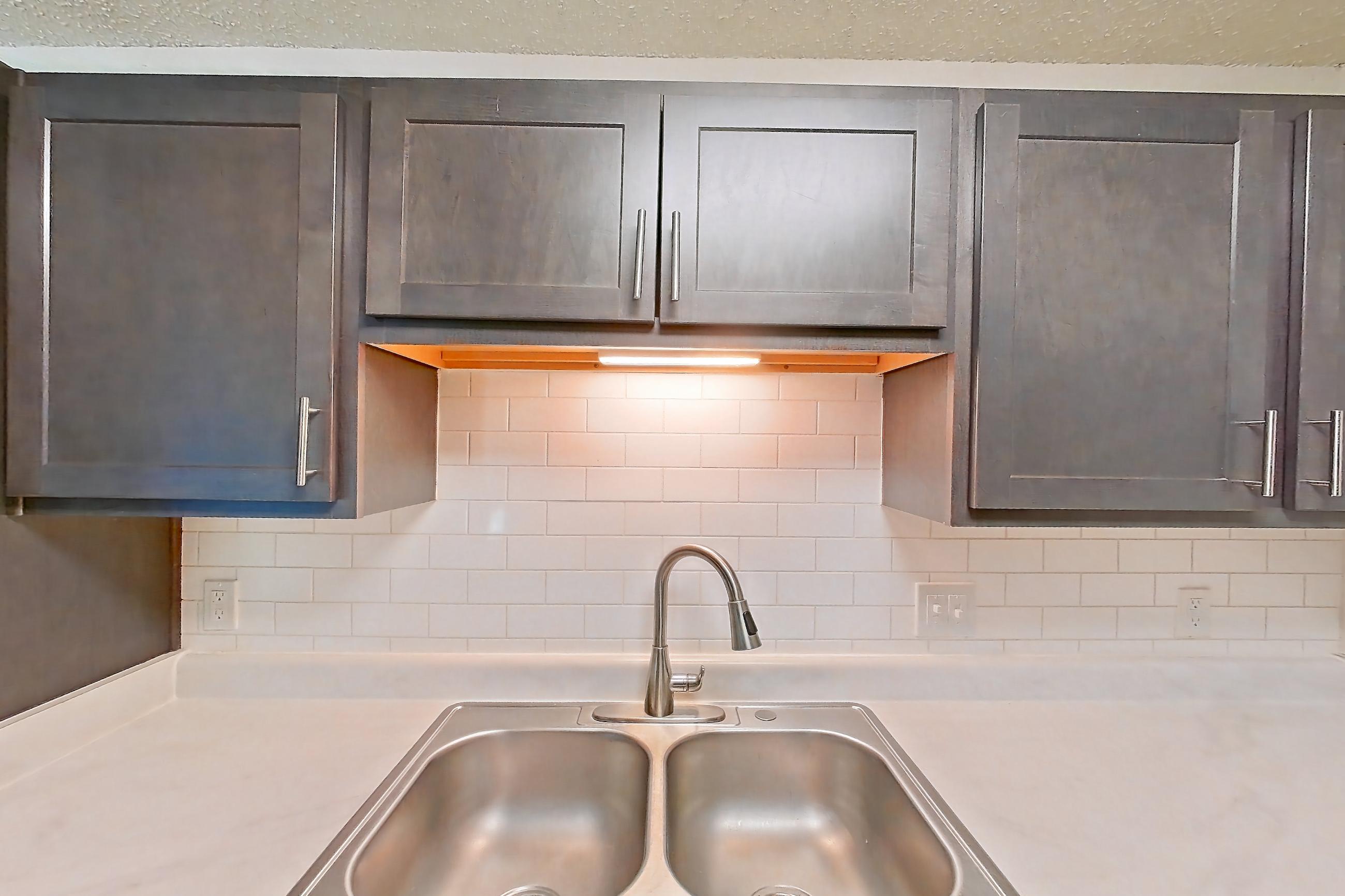 Kitchen with black appliances, dishwasher, electric range, light countertops, light wood-finish flooring, oven/range, refrigerator, and stainless steel appliances, Apartment 135 at Woodwinds
