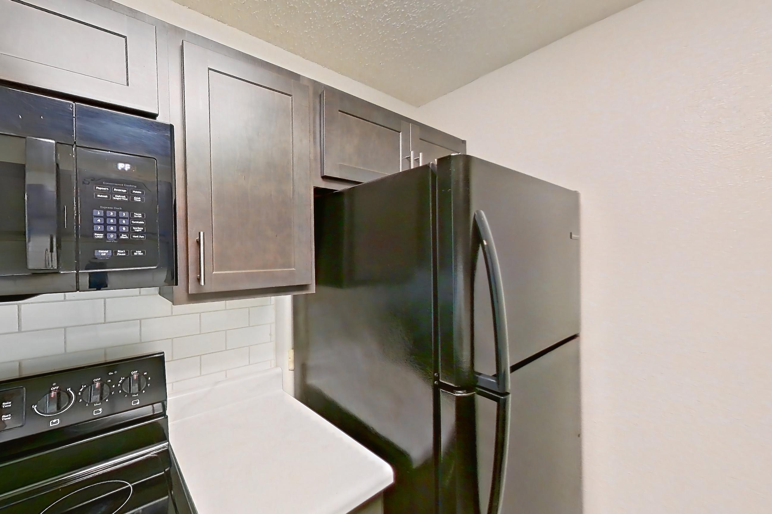 Kitchen with black appliances, dishwasher, electric range, light countertops, light wood-finish flooring, oven/range, range hood, and refrigerator, Apartment 48 at Woodwinds