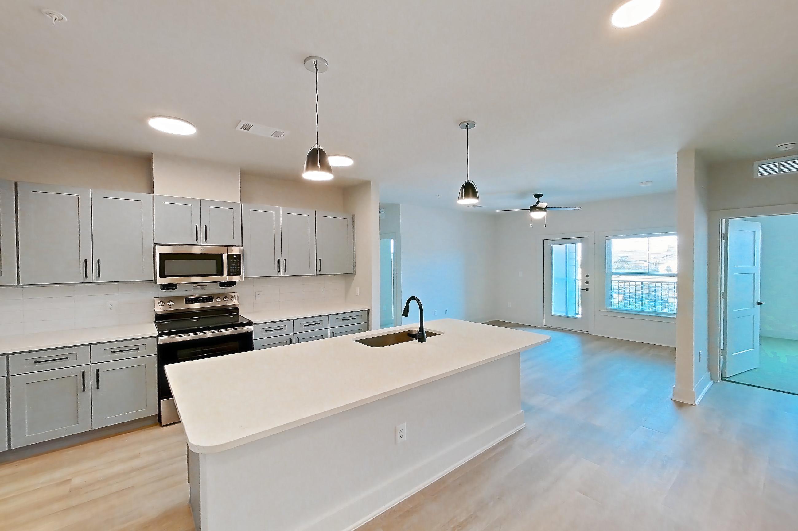 Kitchen corner with electric range, kitchen island, light countertops, light stone countertops, light wood-finish flooring, oven/range, refrigerator, stainless steel appliances, and water & ice dispenser, Apartment 3X at Residences of Siena South