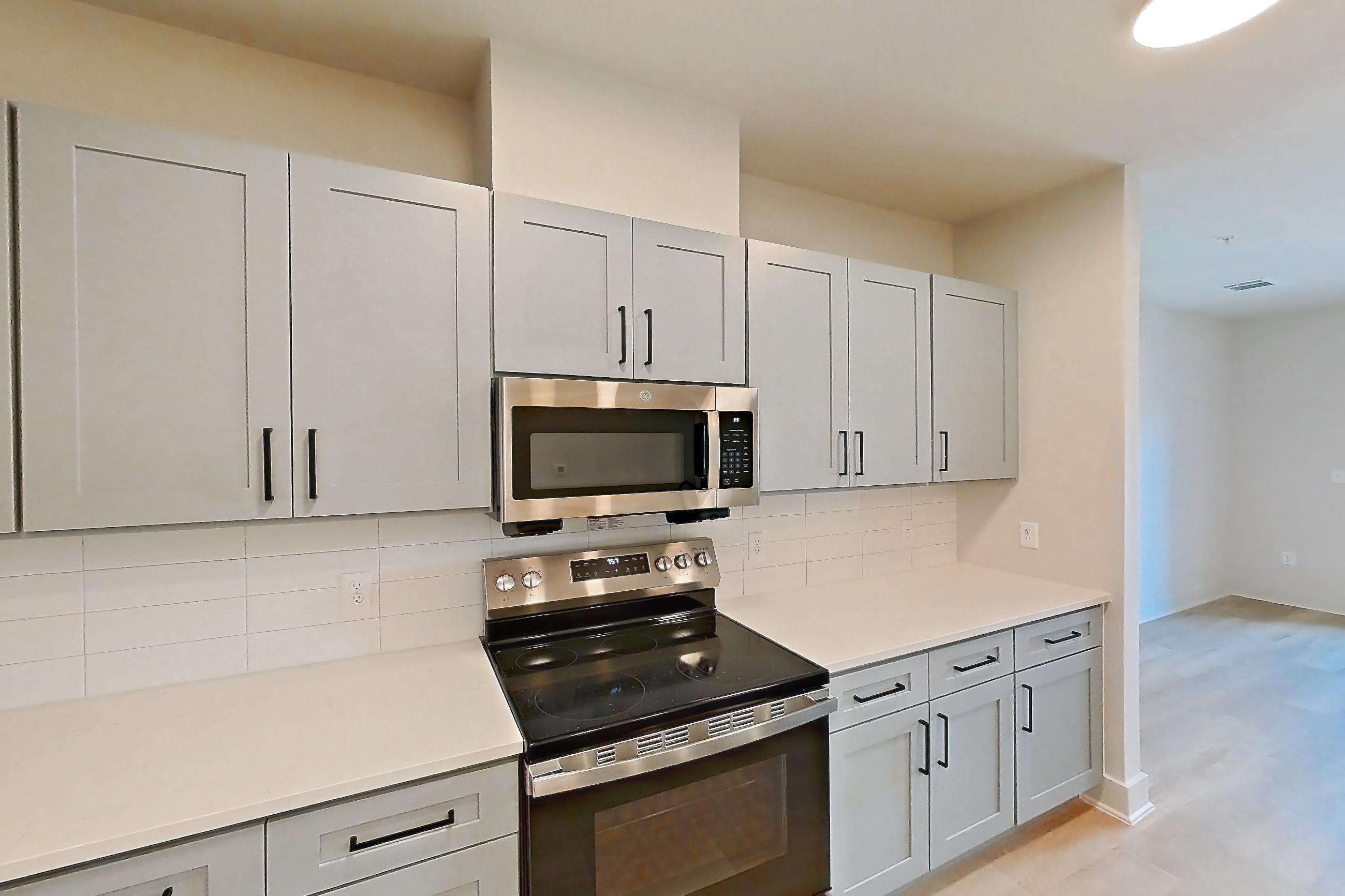 Kitchen with electric range, kitchen island, light countertops, light stone countertops, light wood-finish flooring, microwave, oven/range, refrigerator, stainless steel appliances, and water & ice dispenser, Apartment 3X at Residences of Siena South