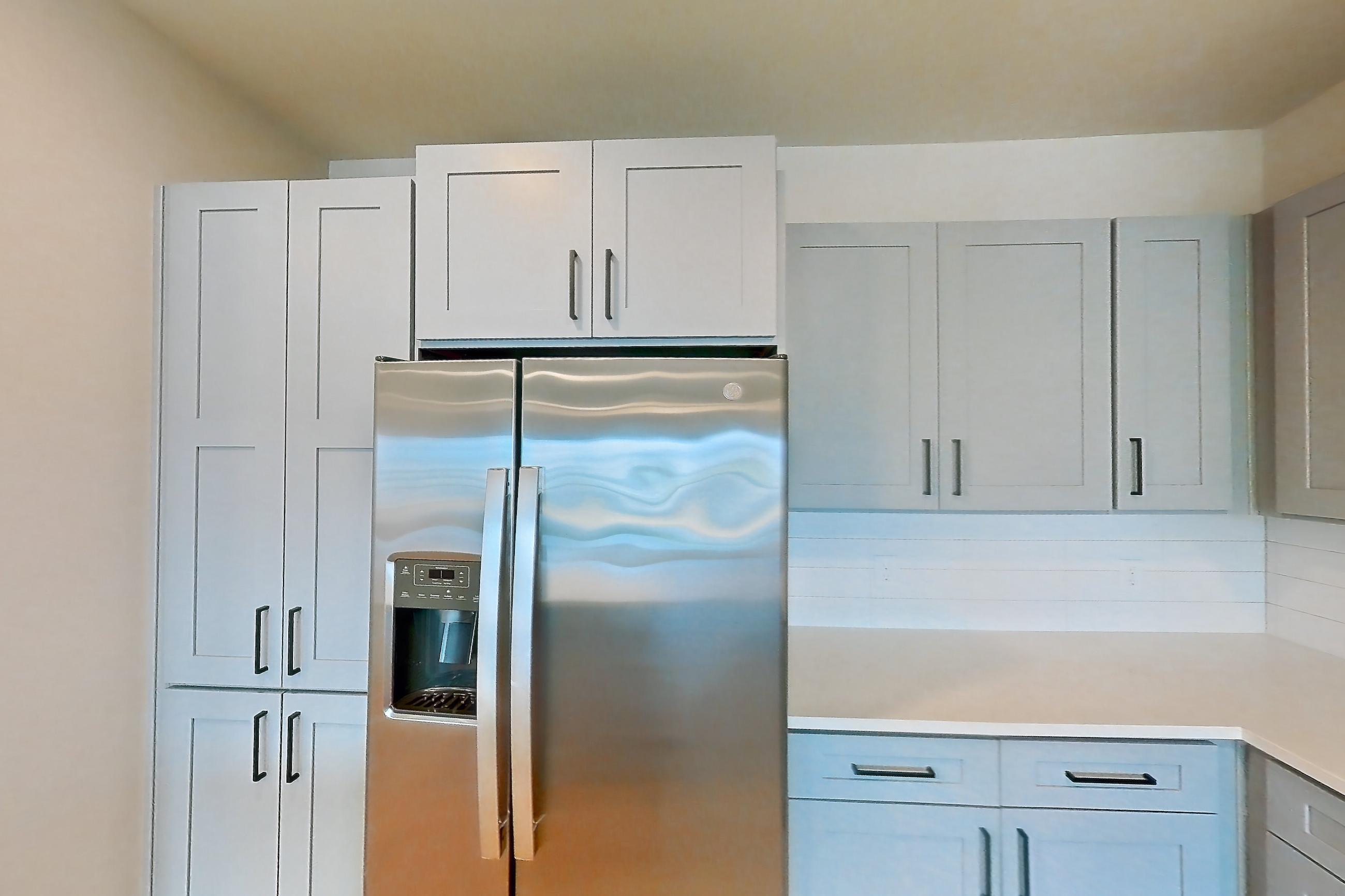 Kitchen with electric range, kitchen island, light countertops, light stone countertops, light wood-finish flooring, microwave, oven/range, refrigerator, stainless steel appliances, and water & ice dispenser, Apartment 3X at Residences of Siena South