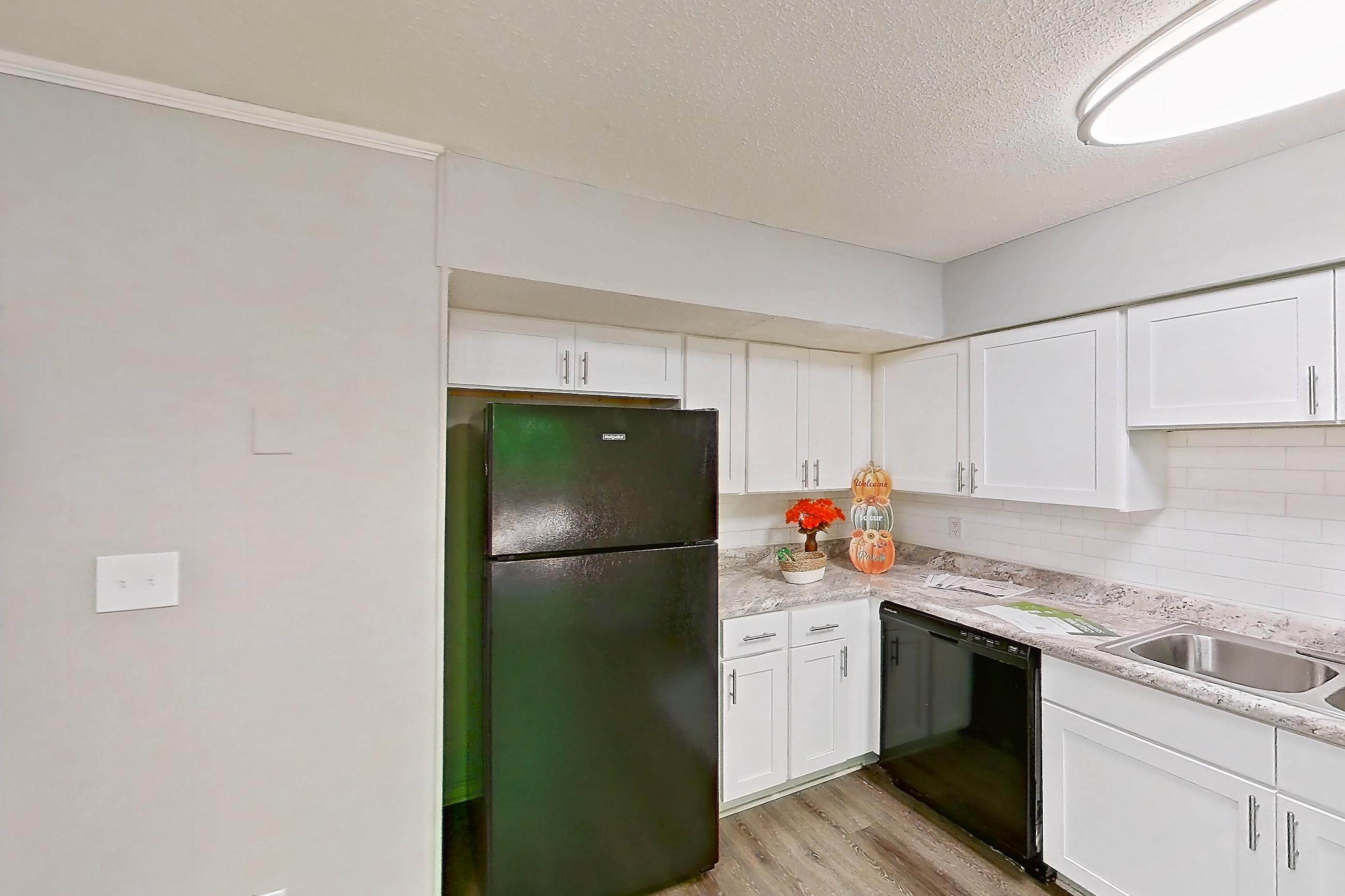 Kitchen with black appliances, dishwasher, electric range, light countertops, light stone countertops, light wood-finish flooring, microwave, oven/range, and refrigerator, Apartment 827B at Carriage House & Azalea
