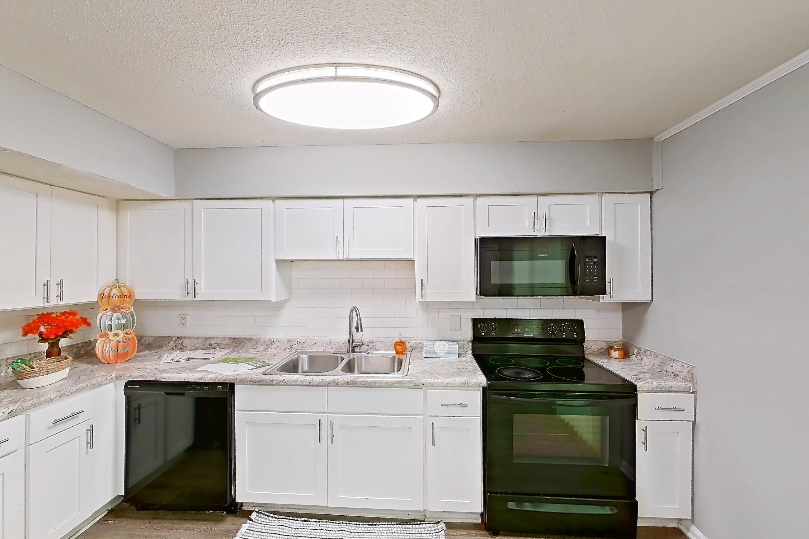 Kitchen with black appliances, dishwasher, electric range, light countertops, light stone countertops, light wood-finish flooring, microwave, oven/range, and refrigerator, Apartment 827B at Carriage House & Azalea