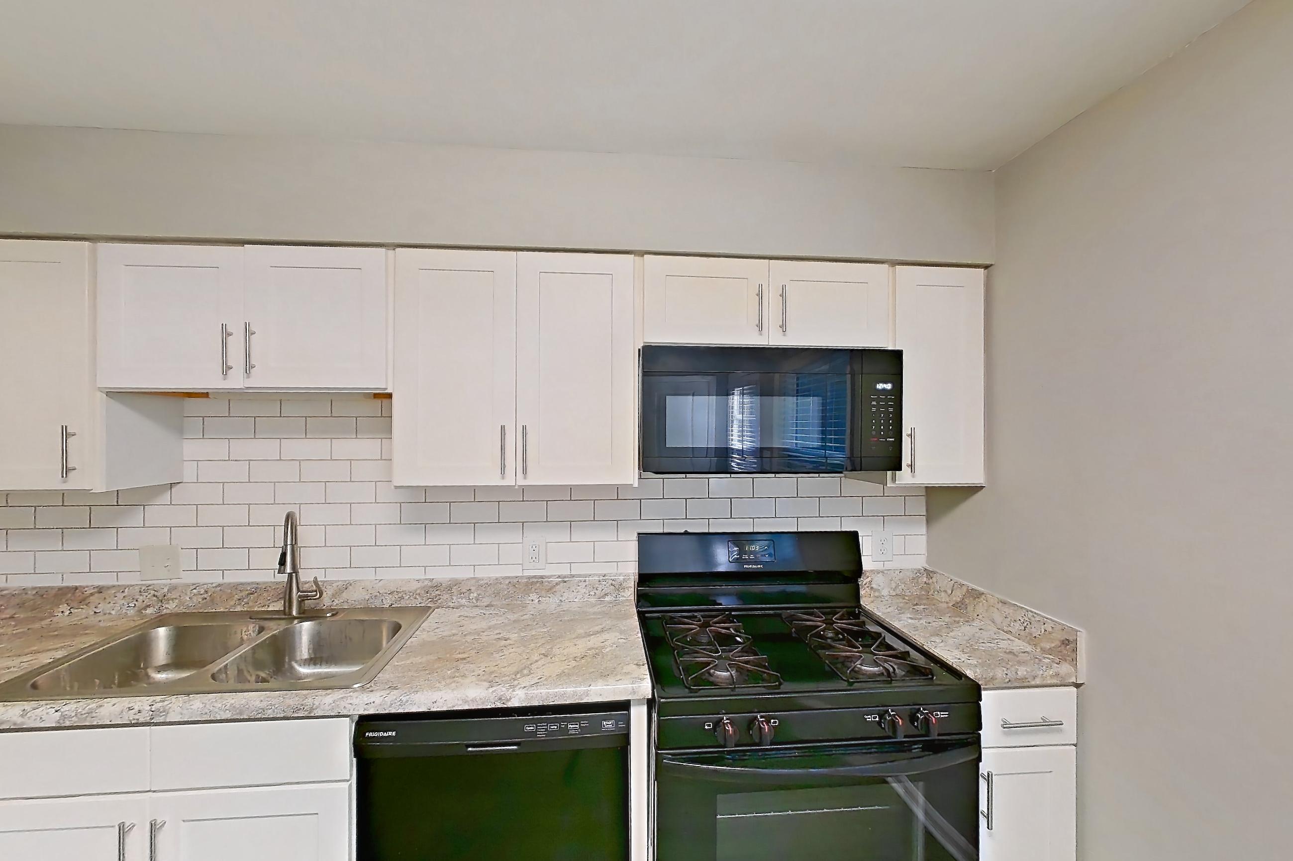 Kitchen with black appliances, dark wood-finish flooring, dishwasher, gas range, light countertops, microwave, oven/range, and refrigerator, Apartment 1260I at Carriage House & Azalea