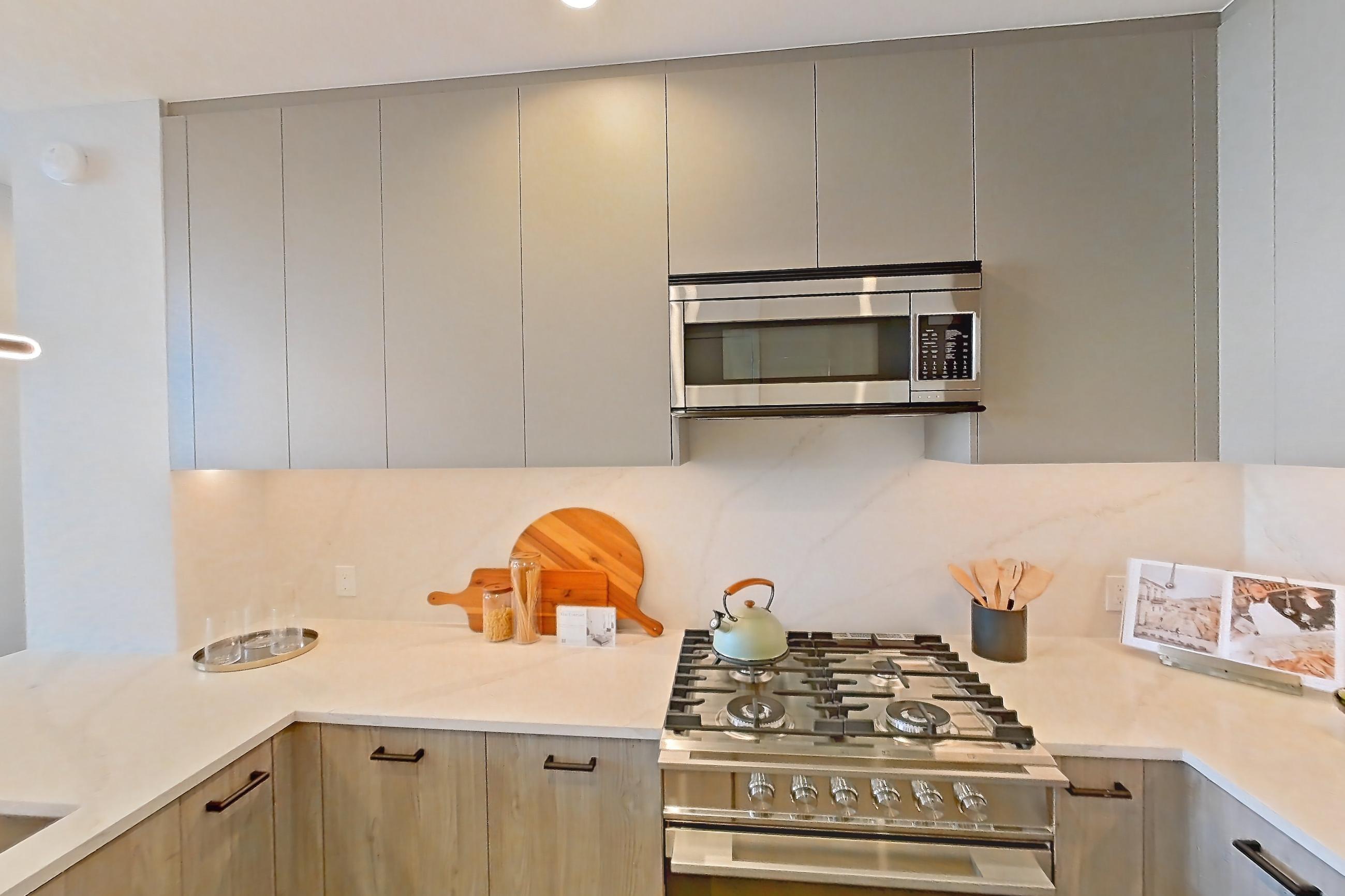 Kitchen with gas range, light countertops, light stone countertops, light wood-finish flooring, microwave, oven/range, and stainless steel appliances, Apartment PH3B at Lumen