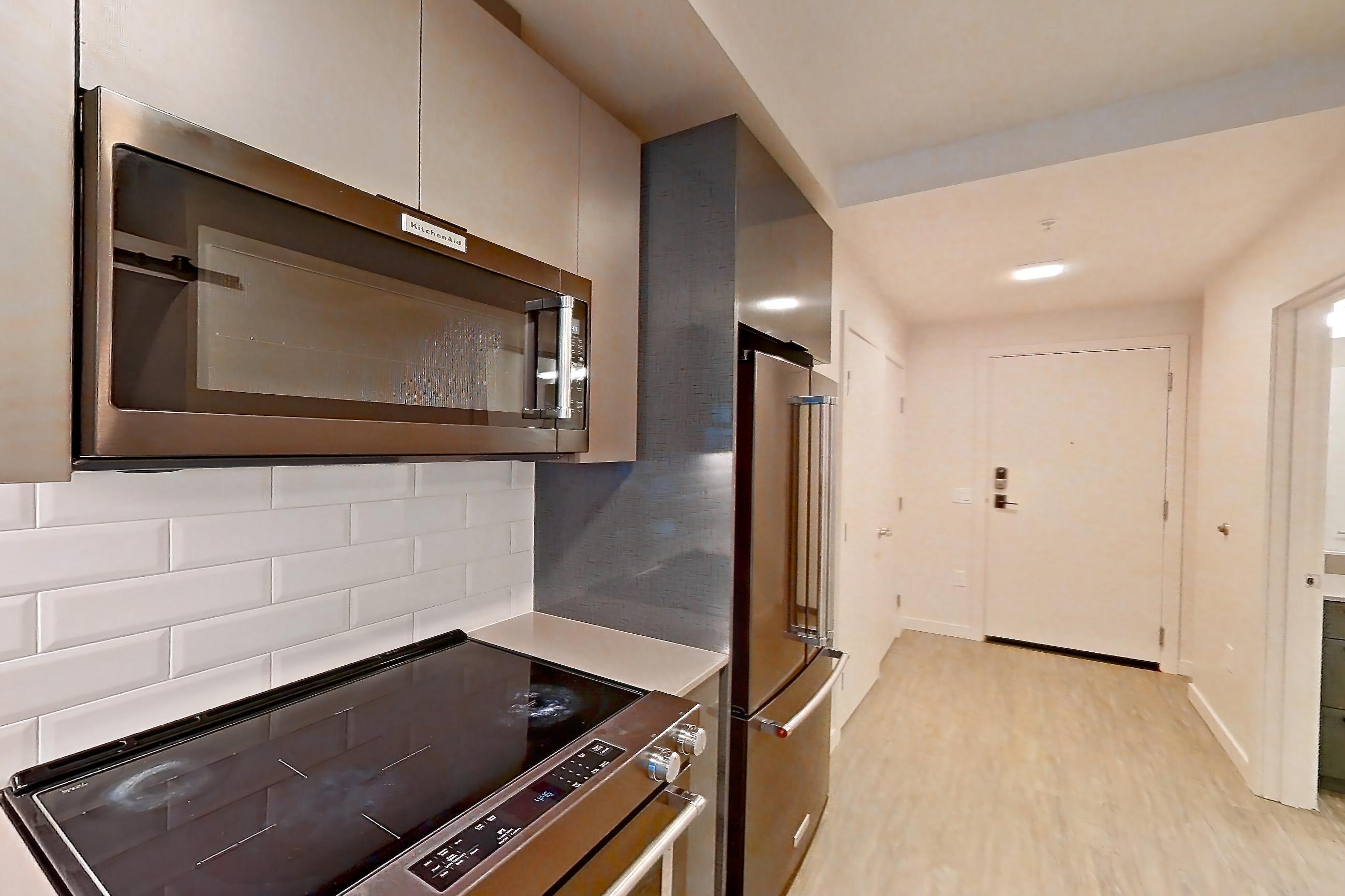 Kitchen with electric range, light countertops, light stone countertops, light wood-finish flooring, oven/range, refrigerator, and stainless steel appliances, Apartment 107 at Chroma