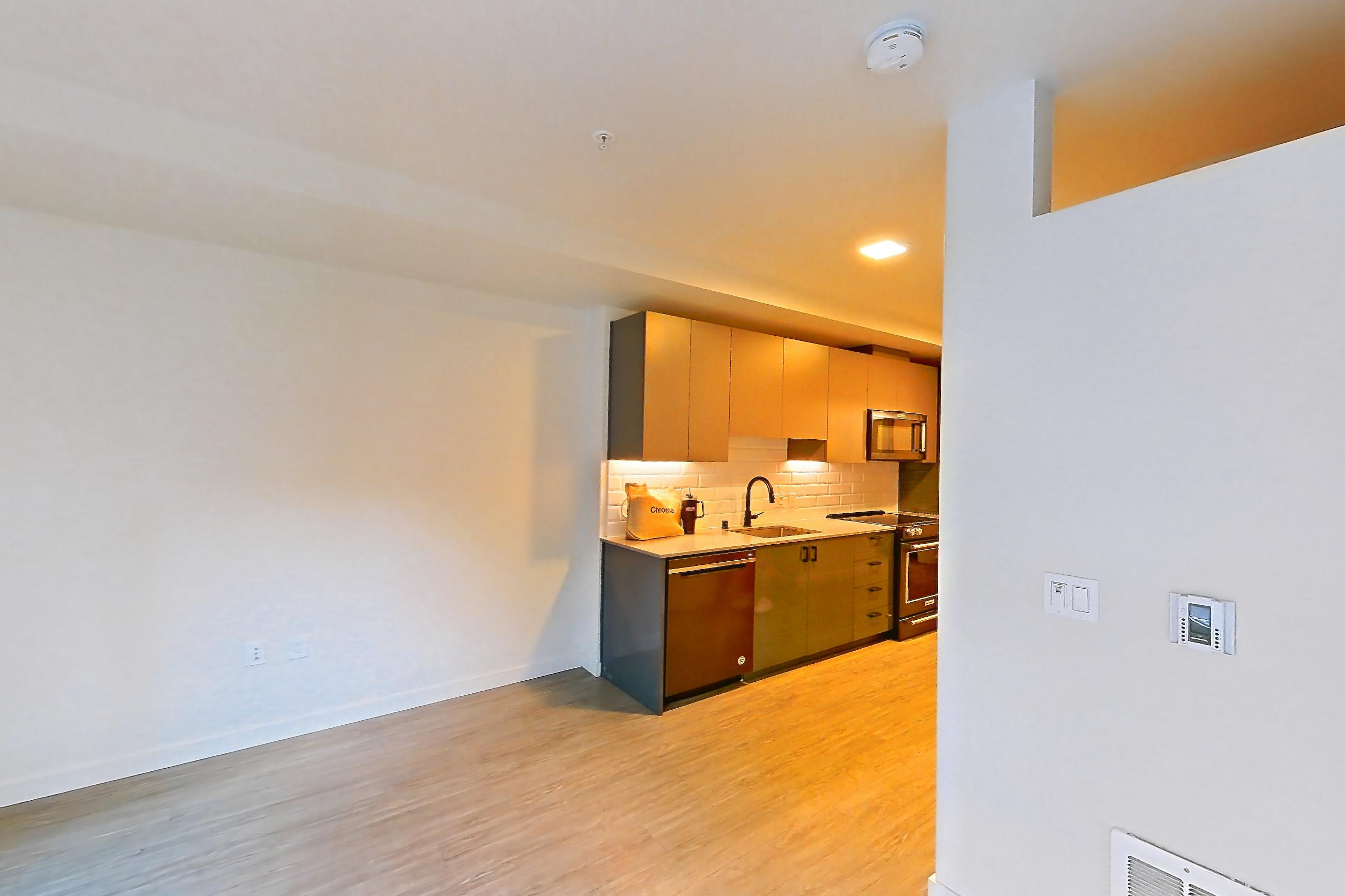 Living room with dishwasher, light wood-finish flooring, and stainless steel appliances, Apartment 107 at Chroma
