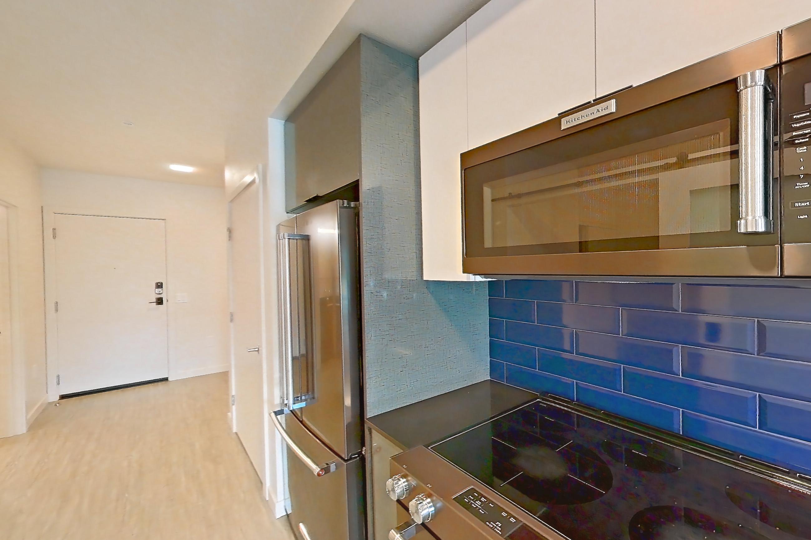 Kitchen with dark countertops, electric range, light countertops, light wood-finish flooring, microwave, oven/range, refrigerator, and stainless steel appliances, Apartment 408 at Chroma